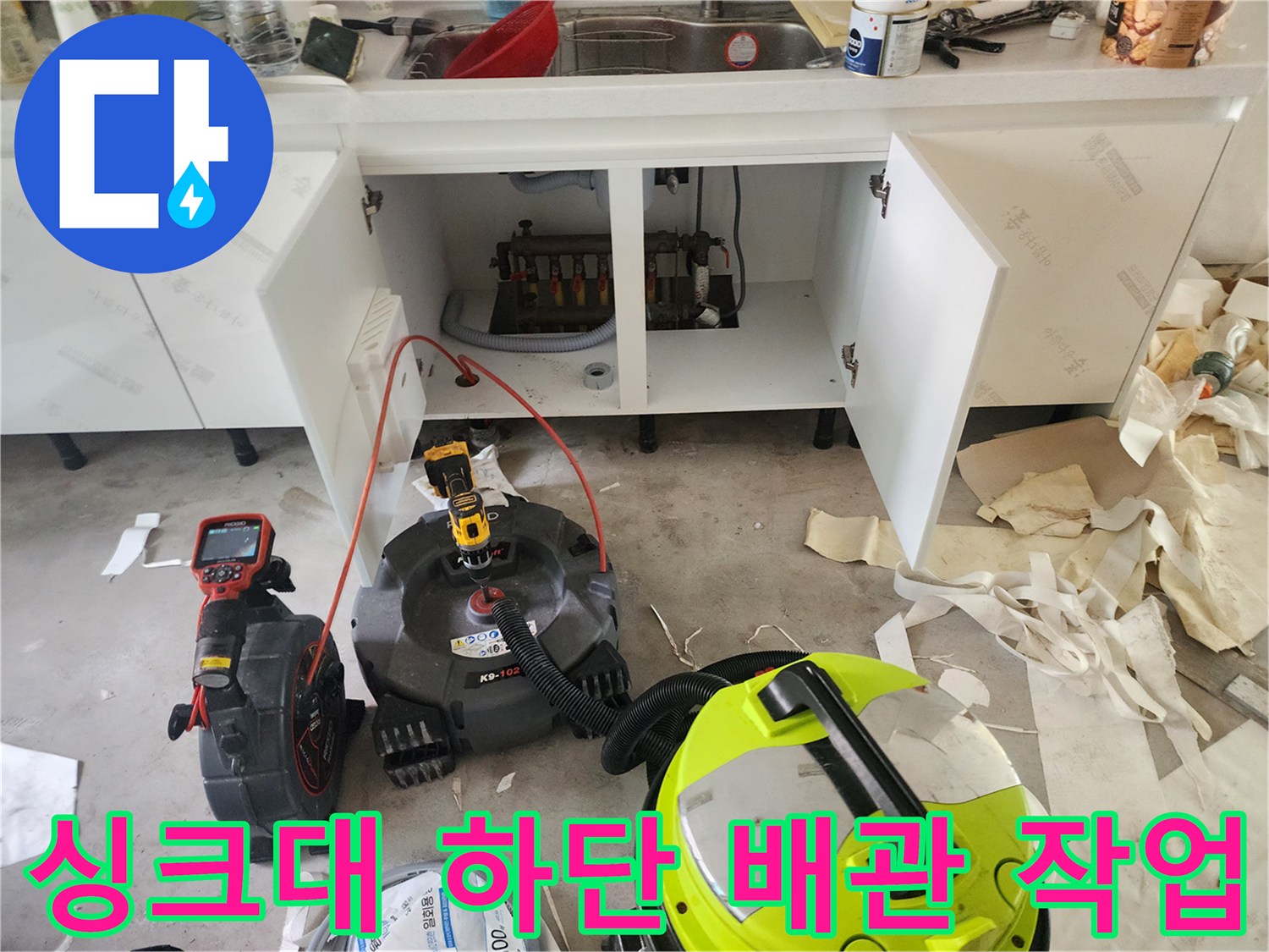 열려 있는 싱크대 하부장 내부와 배관 점검을 위해 준비된 장비들입니다.