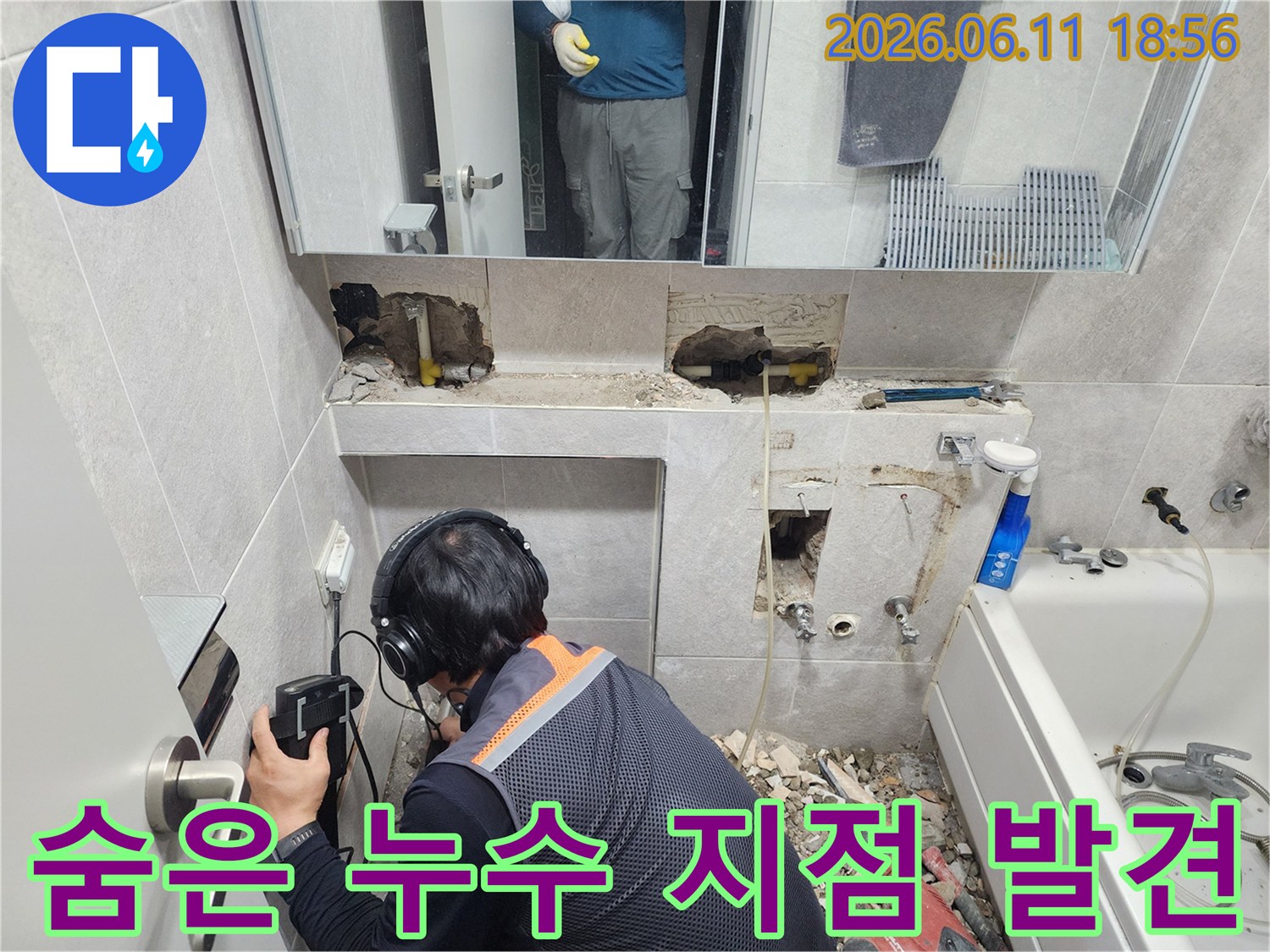 전문가가-누수 탐지 장비를 사용하여-욕실 벽면의-미세한 누수음을 듣고 있는 현장
