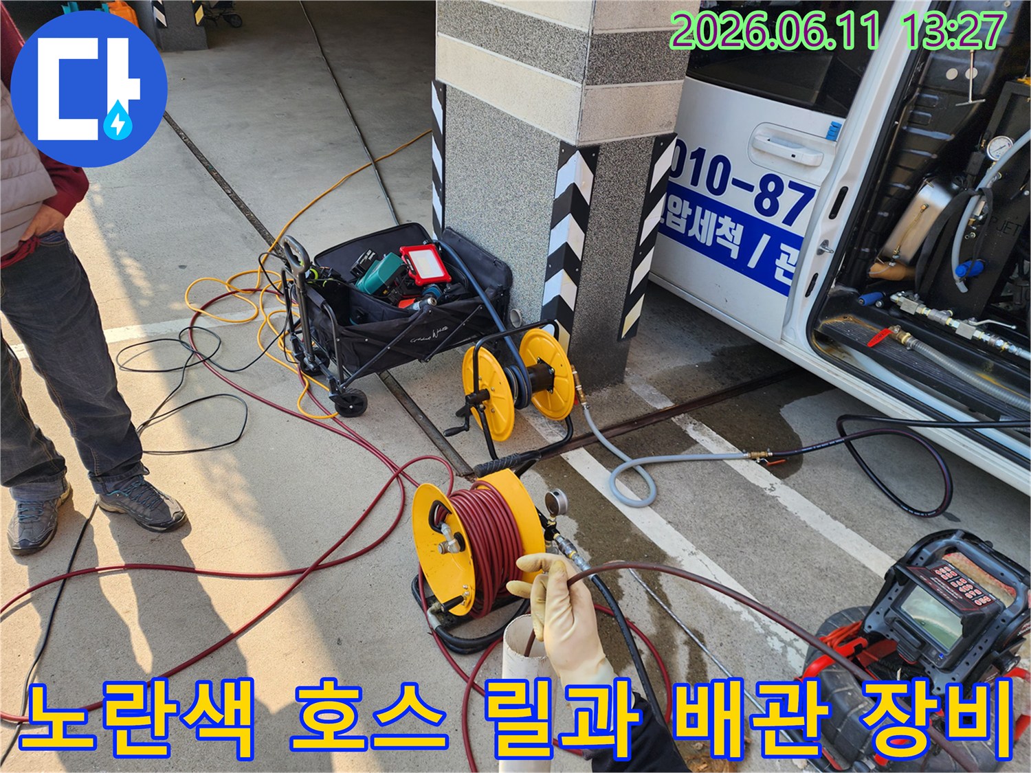 배관 세척을 위해 차량 근처에 배치된 노란색 호스 릴과 작업 도구들