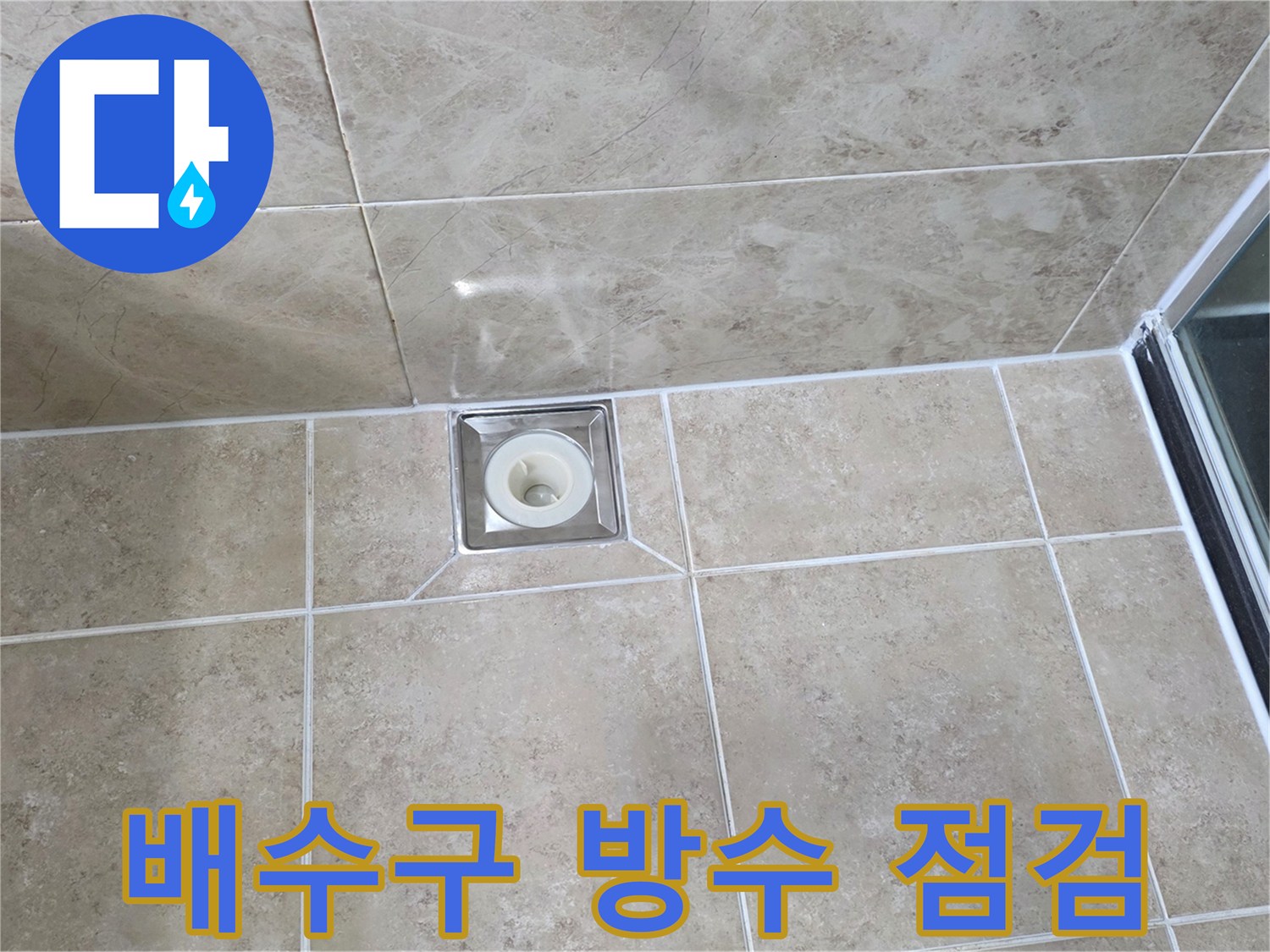 베이지색 타일 바닥에 설치된-금속 사각 배수구의 모습으로-주변 줄눈과 타일의 상태를 점검하는 이미지입니다