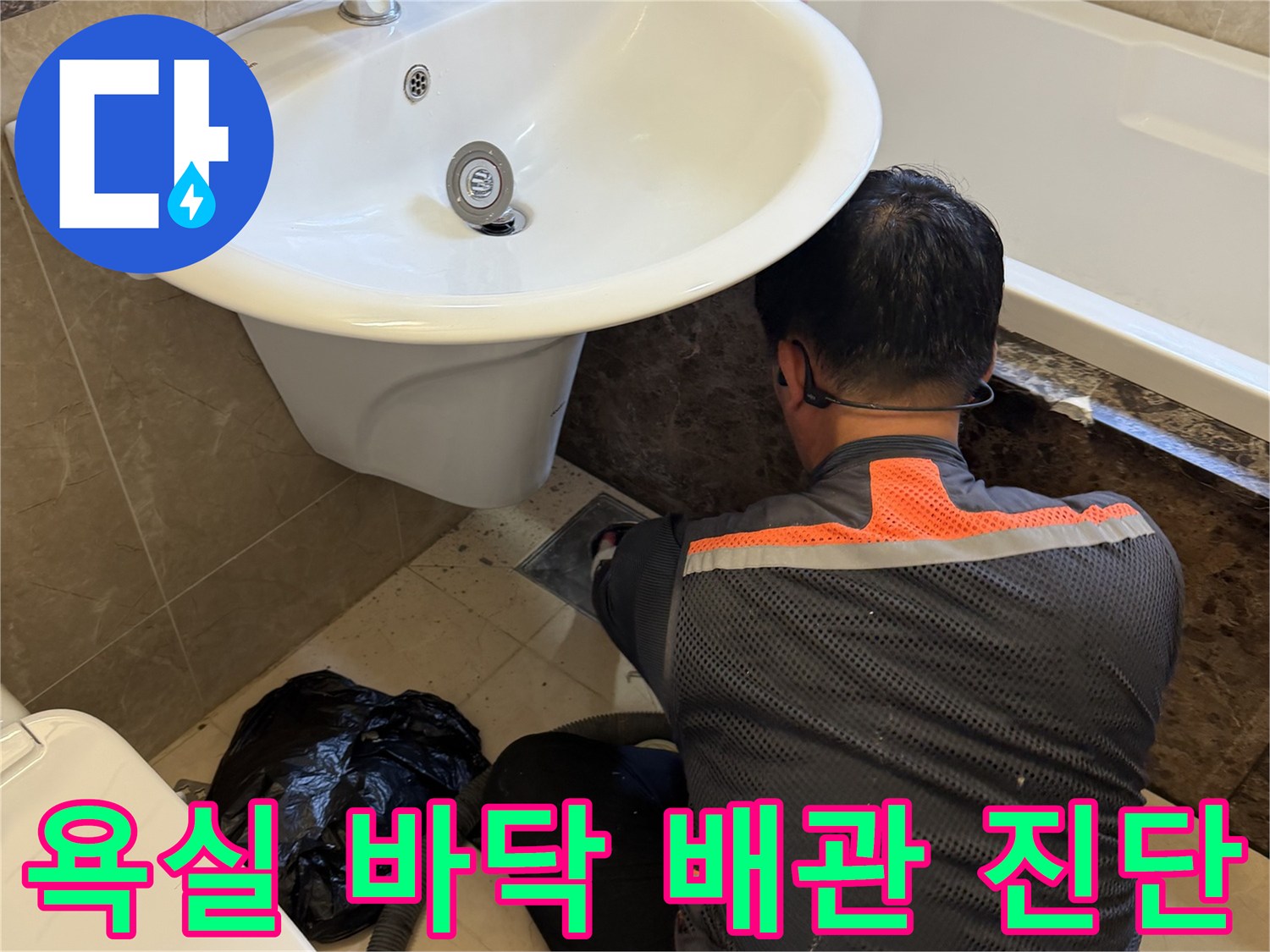 엔지니어가 세면대 아래쪽 좁은 공간에서 배수구 상태를 점검하고 있습니다.