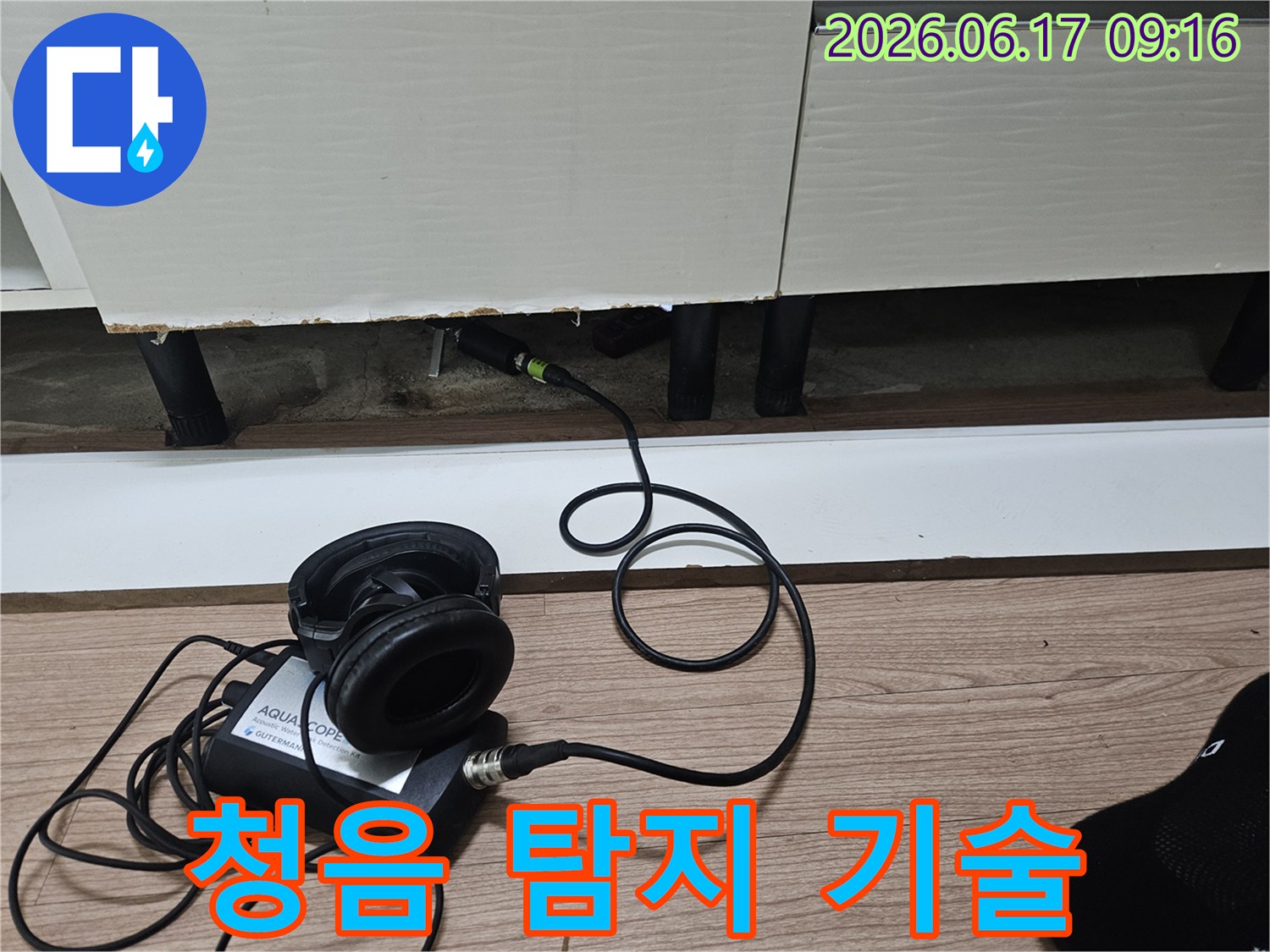 누수 탐지 엔지니어가-청음식 장비를 사용하여-싱크대 하부 배관의 누수음을 탐지하는 기술적인 모습