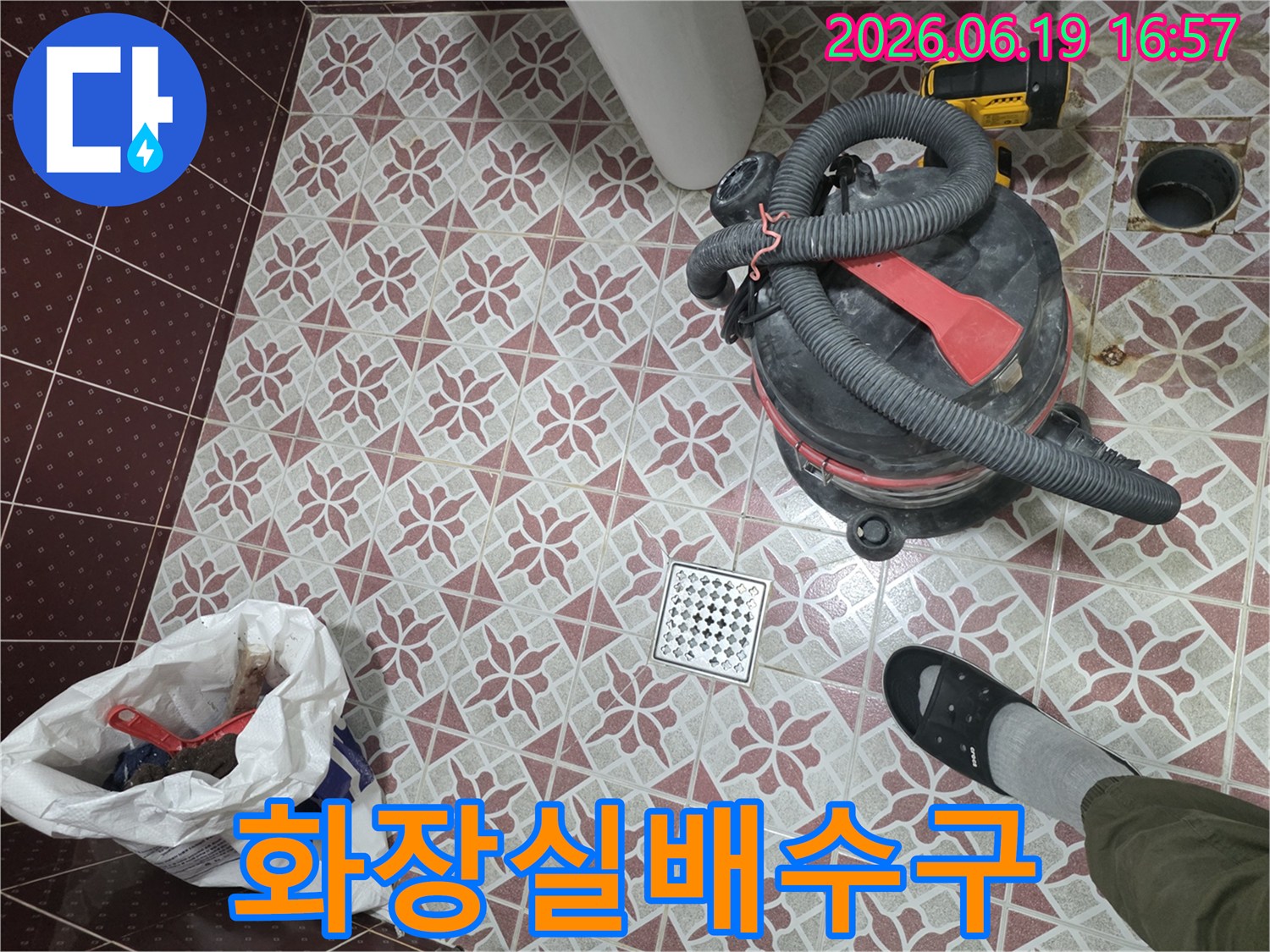 물기 제거를 위해 사용된-산업용 습식 청소기가-욕실 바닥에 놓여 있고-배수구와-작업자의 발이 함께 보이는 장면