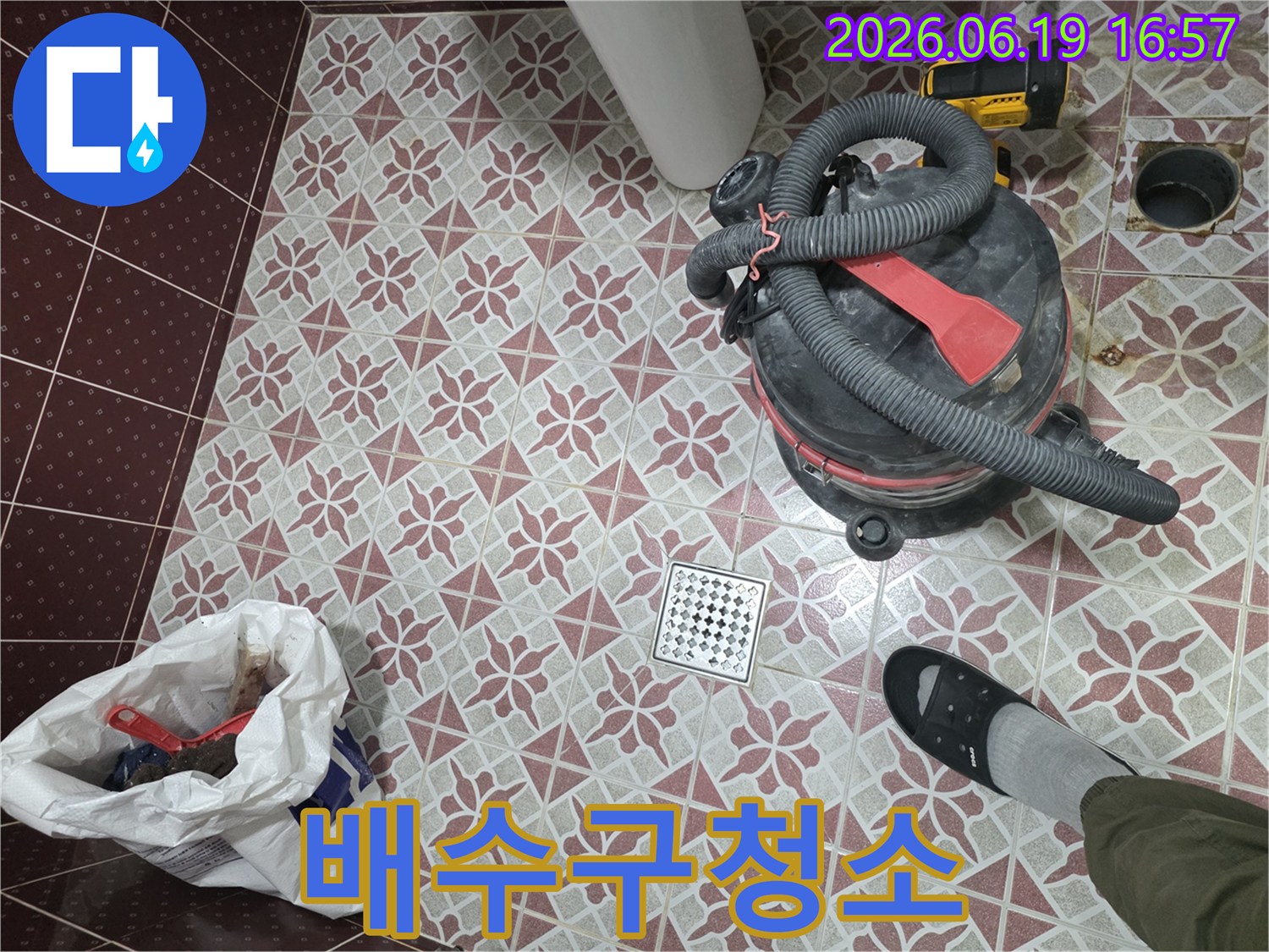 욕실 바닥 타일 위에서 누수 공사 후 물기를 제거하는 습식 청소기-그리고 배수구-작업자의 발이 보이는 현장 모습
