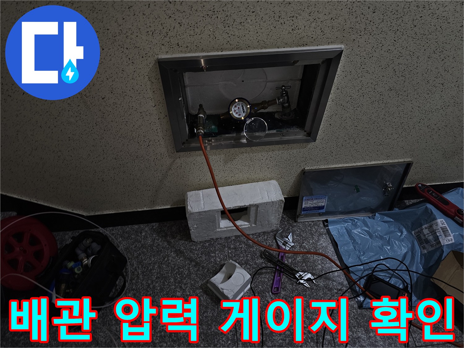 벽면 점검구 내부에 설치된 배관 연결부와 디지털 압력계 이미지입니다.