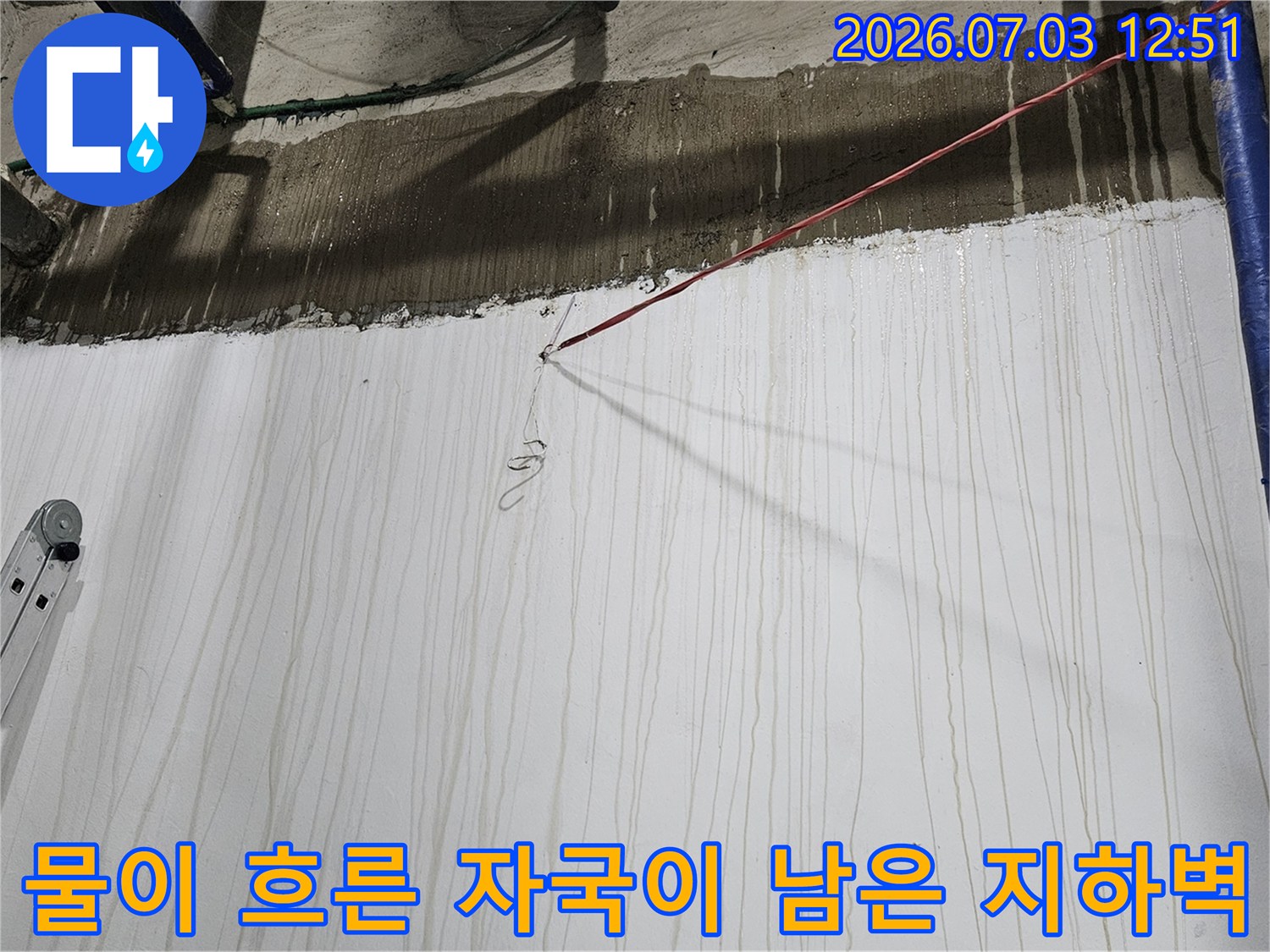 파란색 배관과 사다리가 놓여 있고 벽면에 세로 방향으로 누수 얼룩이 형성된 현장