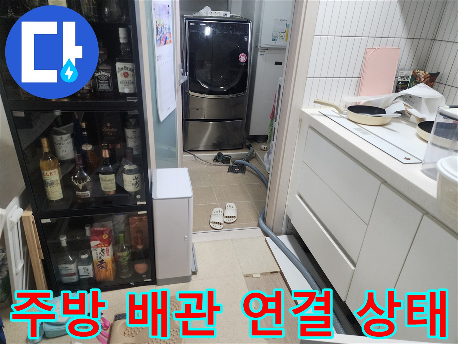 싱크대 하부장 옆으로-세탁기 배수 호스와 바닥 배수구가 위치한 현장 사진입니다.