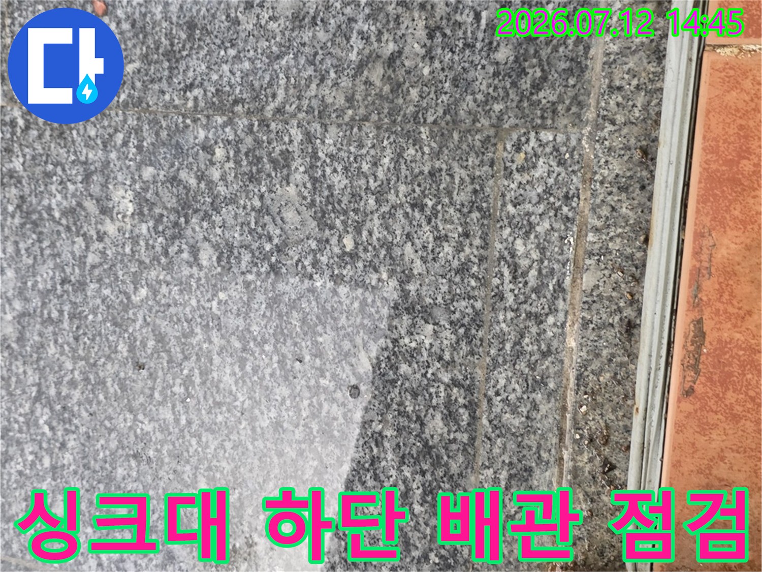 싱크대 하부의 거친 질감의 돌 타일과 노출된 배관 연결 부위 점검 모습