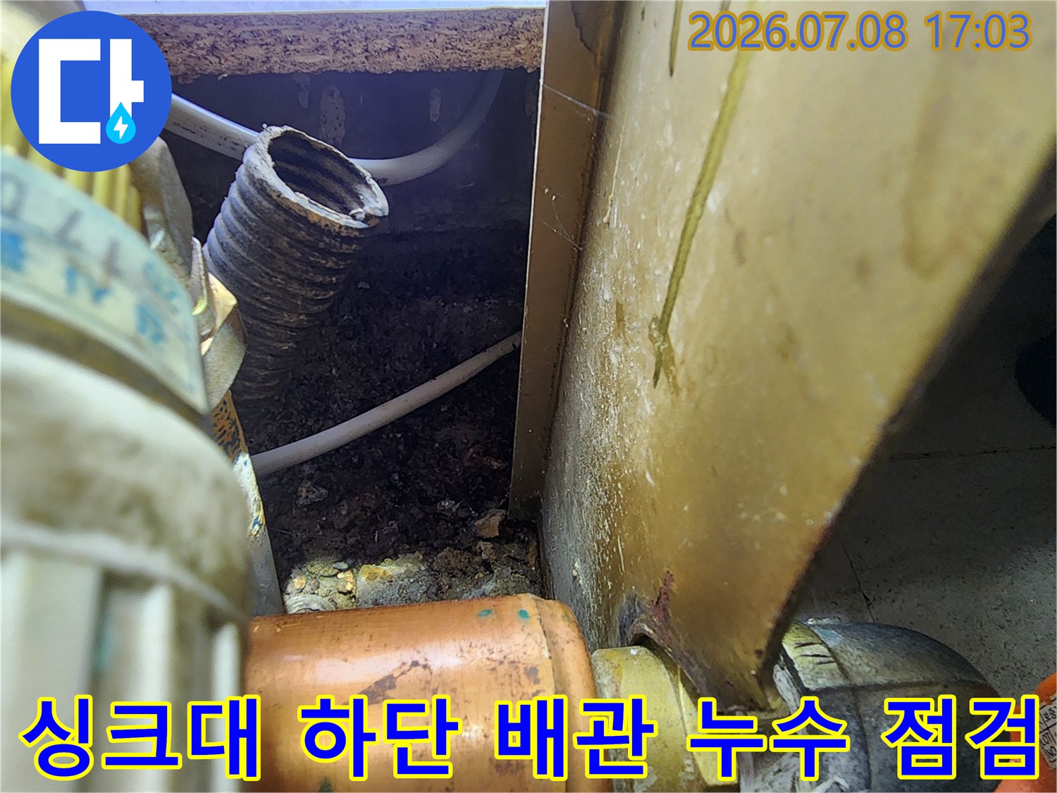 싱크대 하부 공간의 굴곡진 배관과 노출된 관 연결 부위를 점검하는 모습
