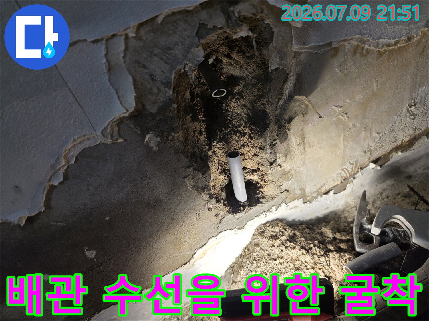 거칠게 파헤쳐진 벽면 너머로 드러난 흰색 배관과 주변의 공사 현장 모습