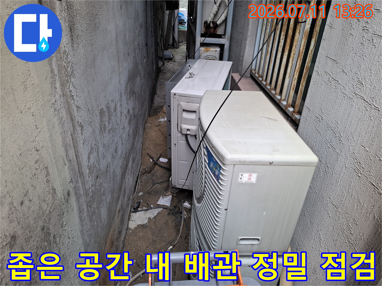 실외기들이 위치한 좁은 통로에서 드레인 배수 호수의 연결 상태를 상세히 확인하는 장면