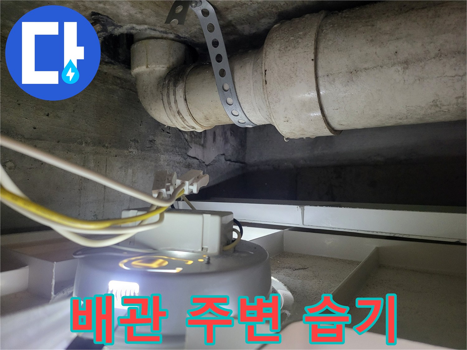 하수관 연결 부근의 금속 밴드와 전선이 노출된 천장 내부 모습입니다.