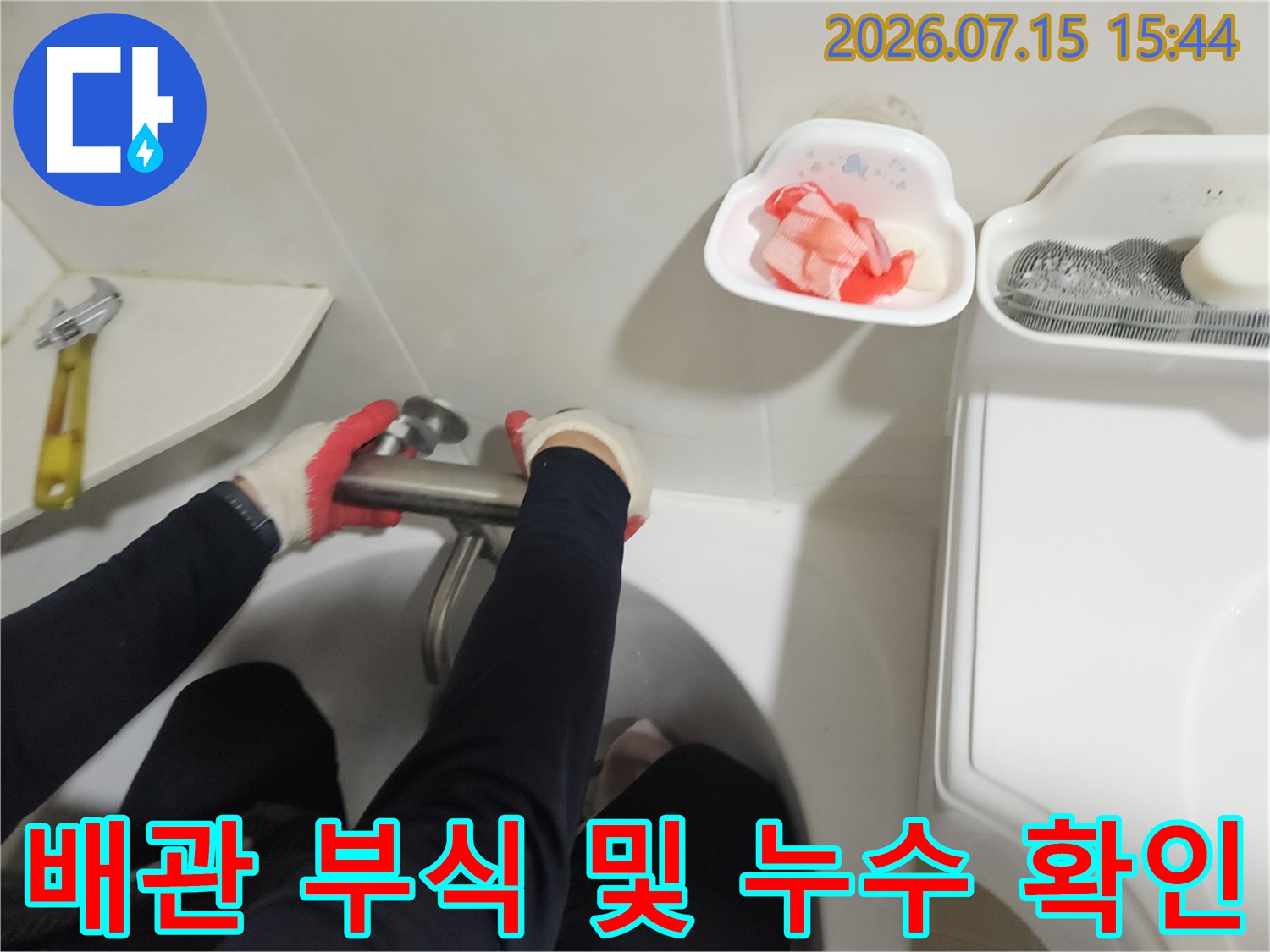 작업자가 세면대 밑 배관 연결부를 손으로 점검하는 장면