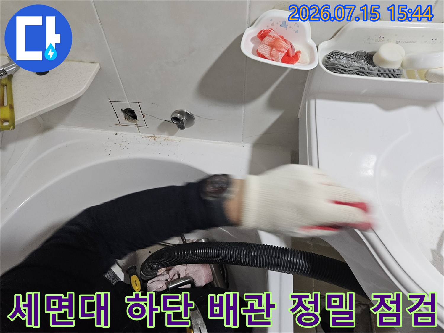 작업자가 장갑을 끼고 세면대 밑에 설치된 배관부를 꼼꼼하게 확인하는 장면