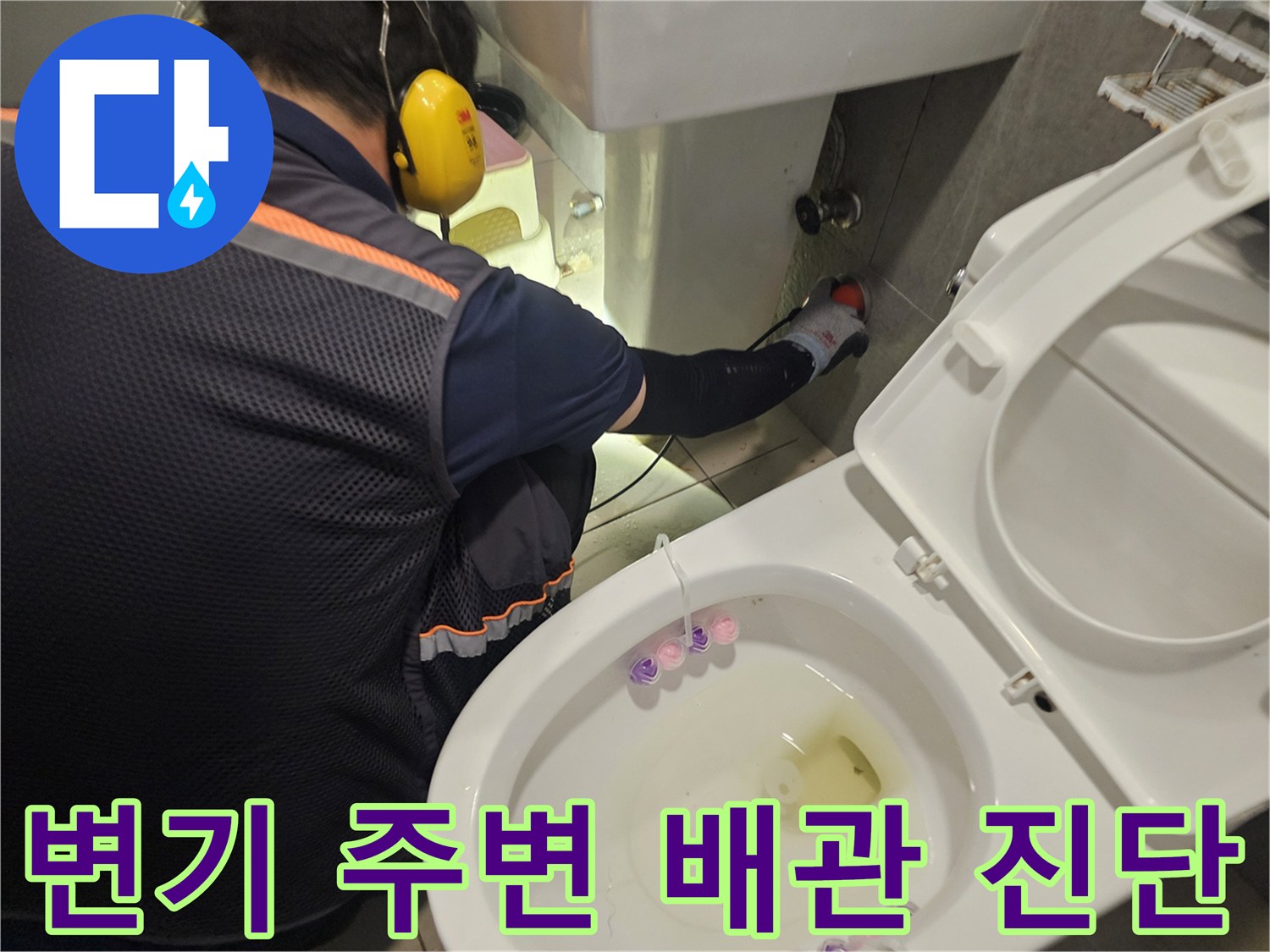 작업자가 변기 뒤쪽 벽면의 배관 연결 부위를 공구로 점검하고 있습니다.