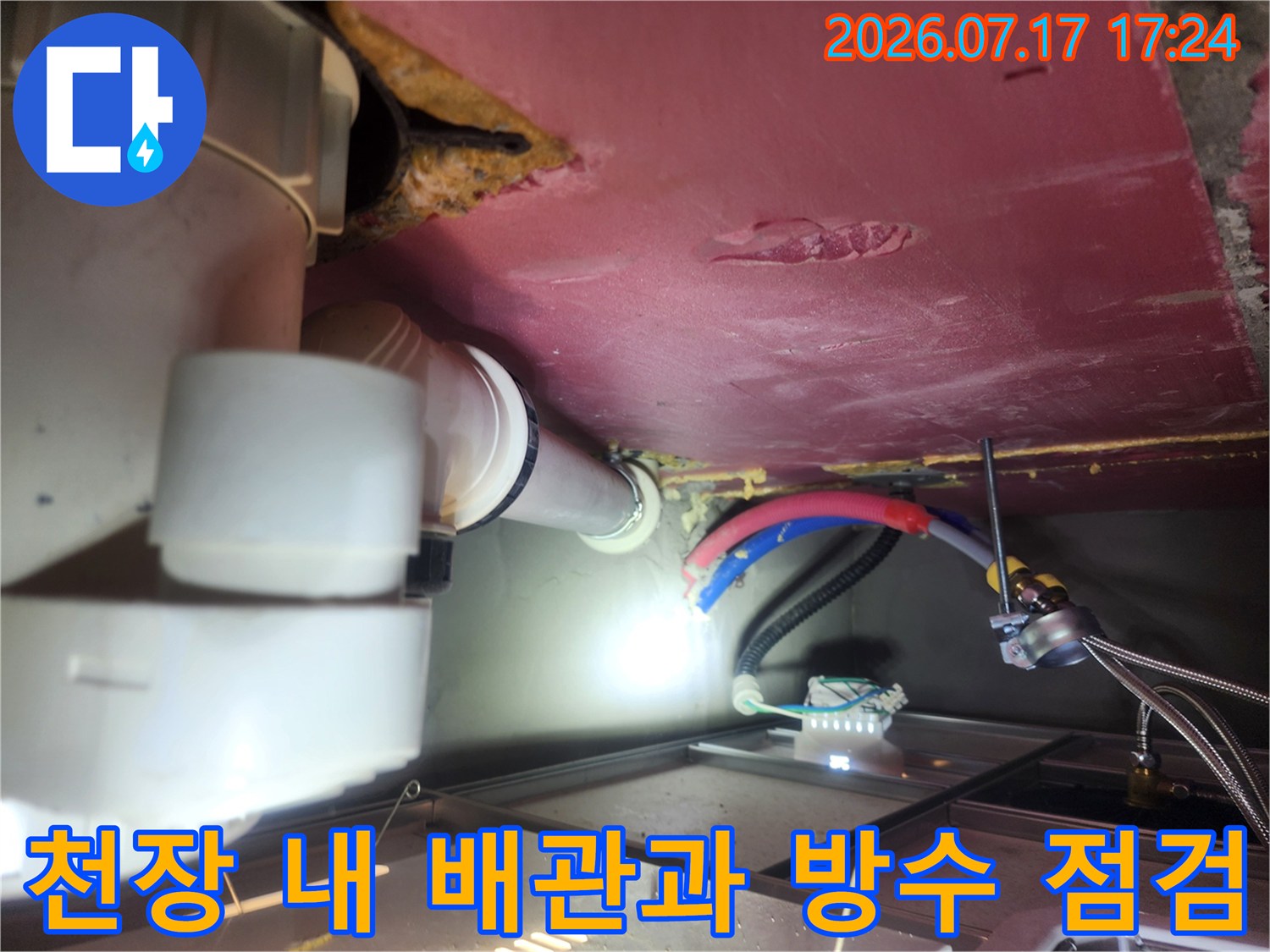 천장 내부를 비추며 배관 연결부와 주변 마감재의 상태를 조사하는 모습