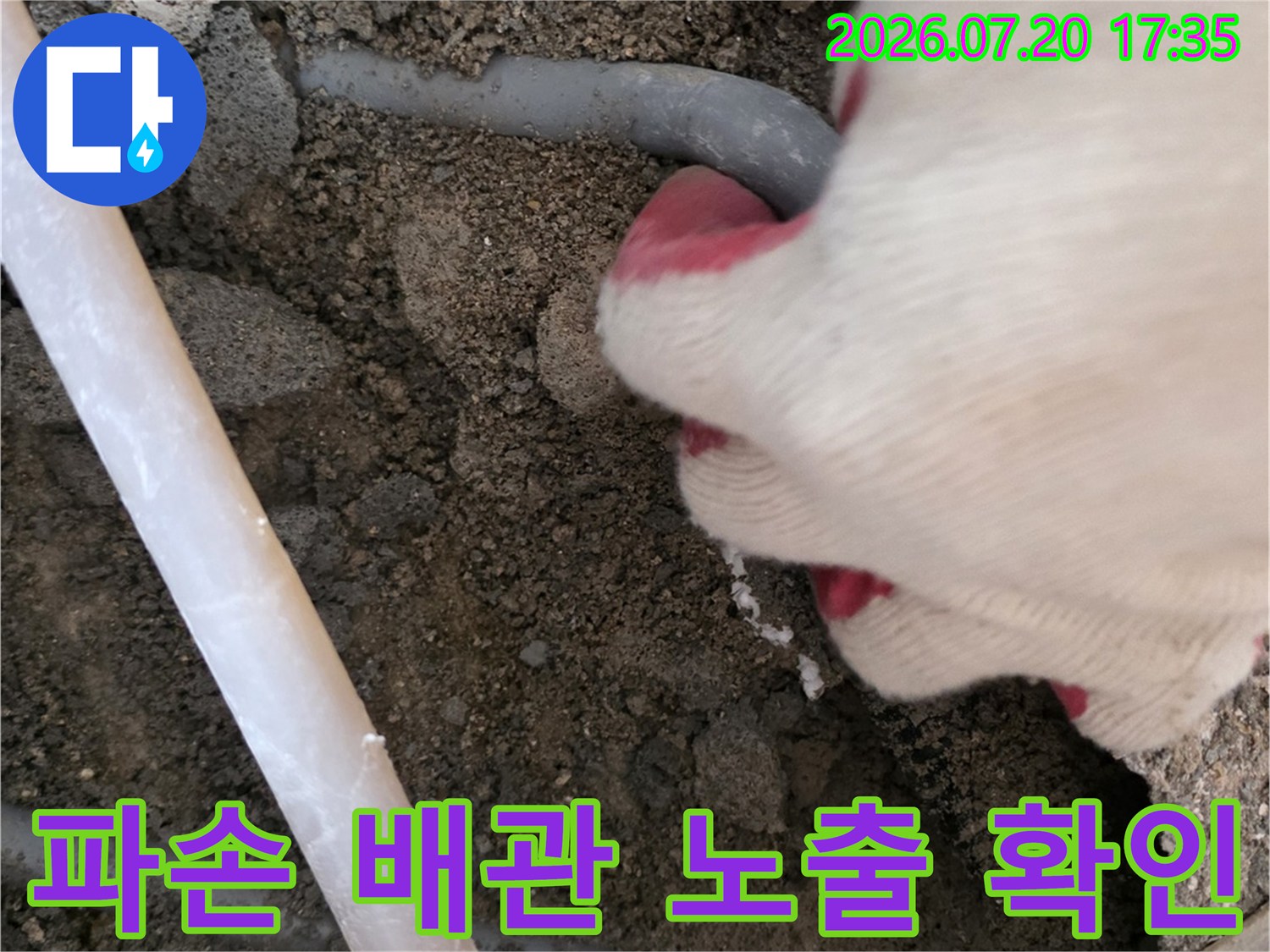 굴착된 지점에서 파손된 회색 배관을 손으로 잡아 누수 부위를 식별하는 모습