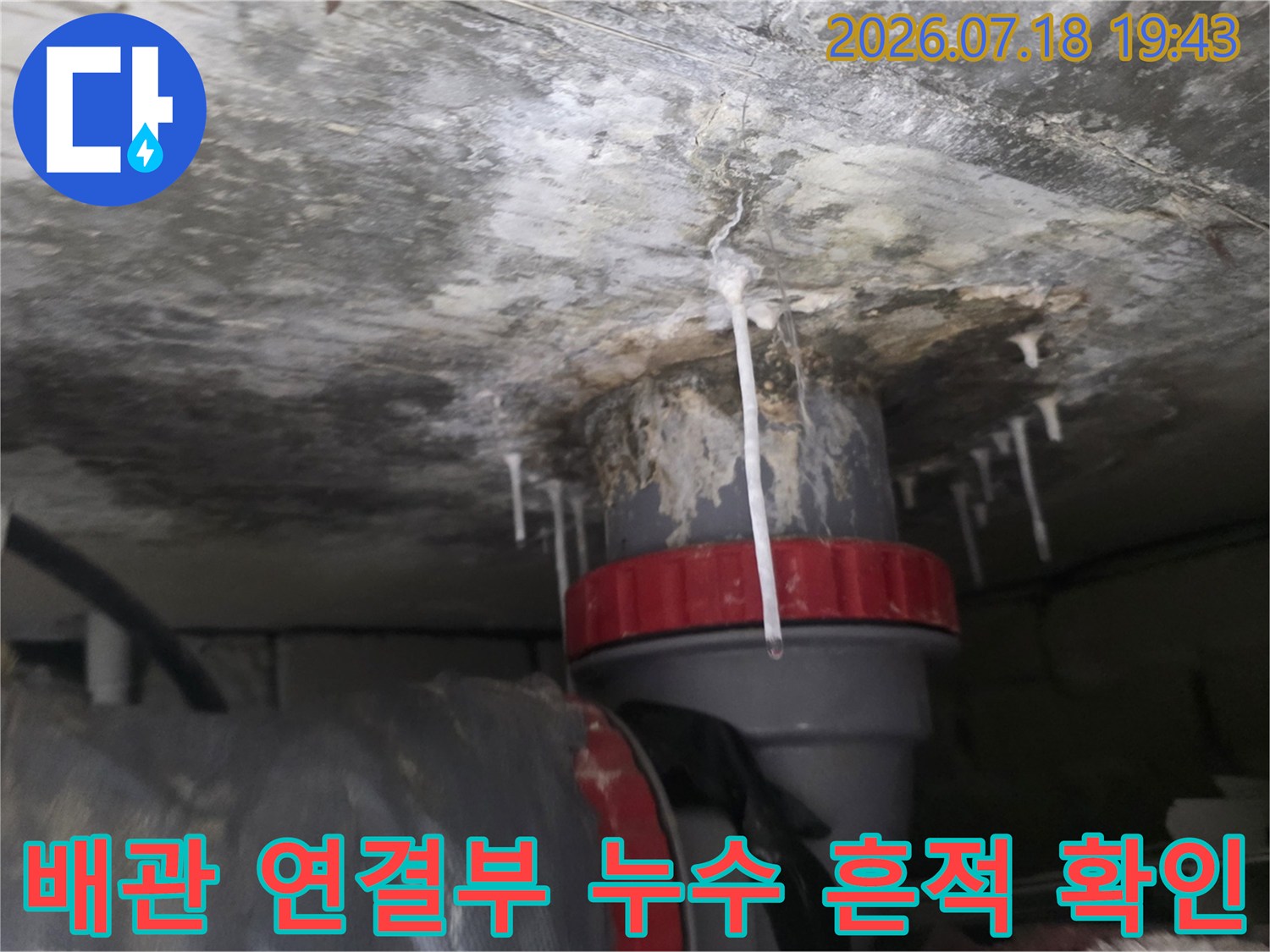 천장 배관 연결 부위에서 누수로 인한 물줄기가 떨어지는 장면