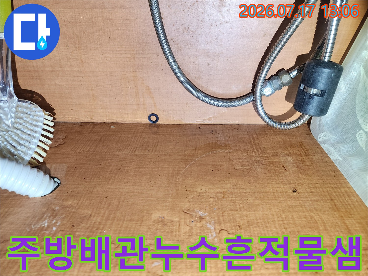 물에 젖어 어둡게 변색된 싱크대 하부장 내부 목재 벽면-금속 및 플라스틱 호스 배치