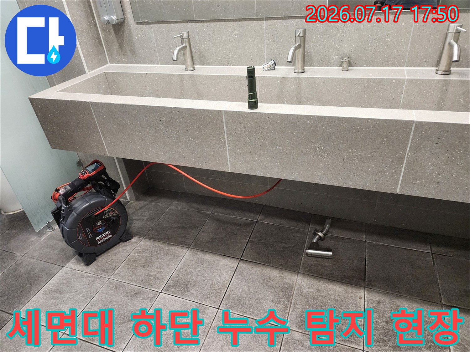 회색 석재 세면대 아래의 금속 배수관과 빨간 선이 연결된 측정 장치