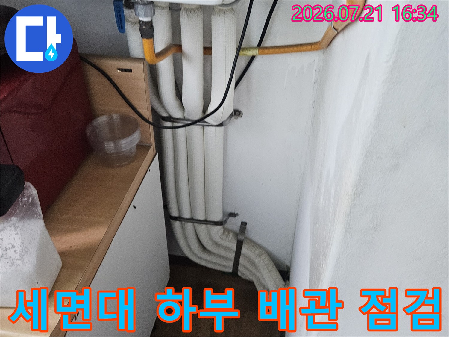 세면대 아래쪽으로 노출된 여러 개의 수도 배관과 연결 부위를 정밀하게 점검하는 모습