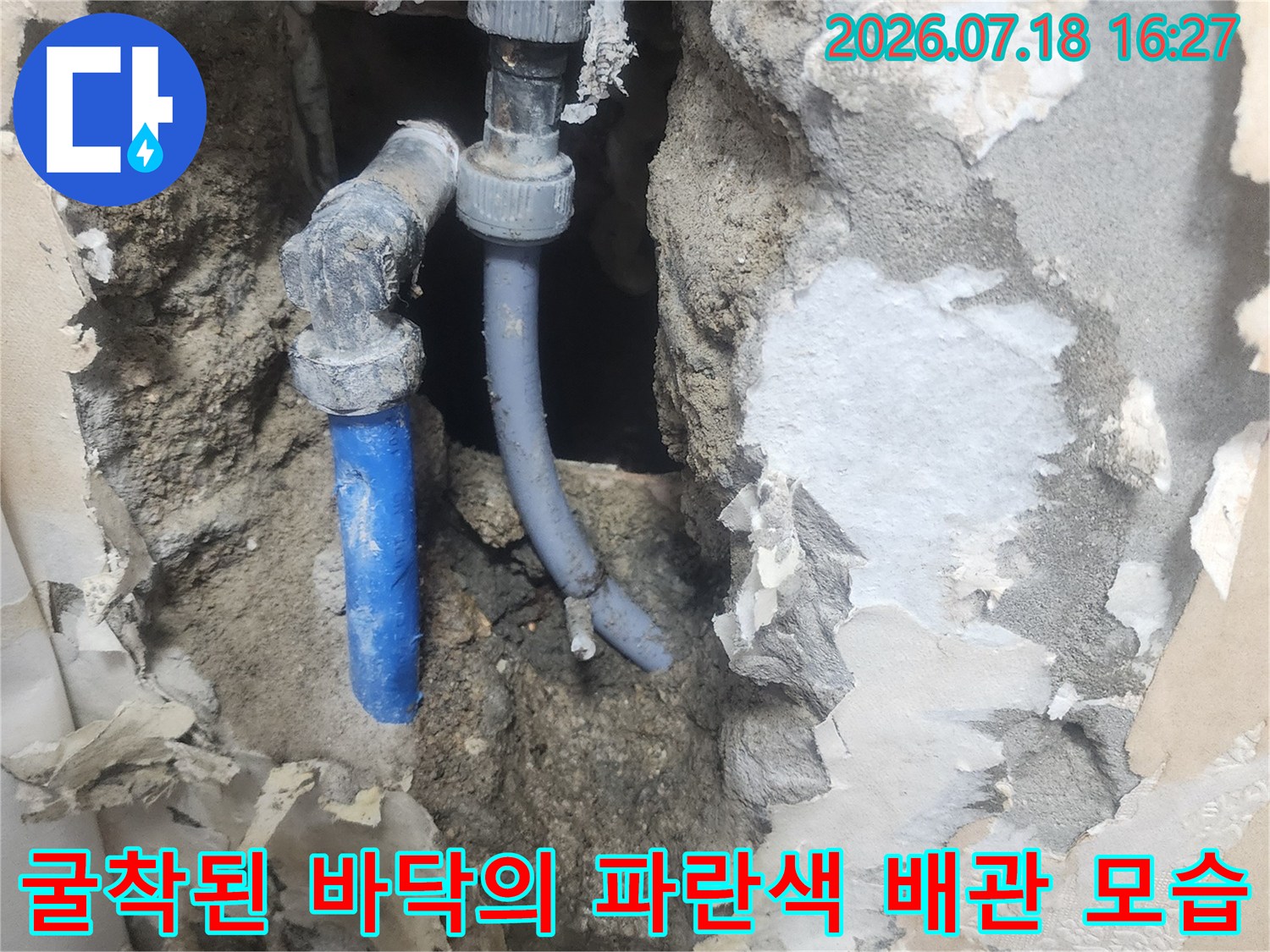 콘크리트 층을 제거하여 드러난 회색 연결부와 파란색 수도 파이프