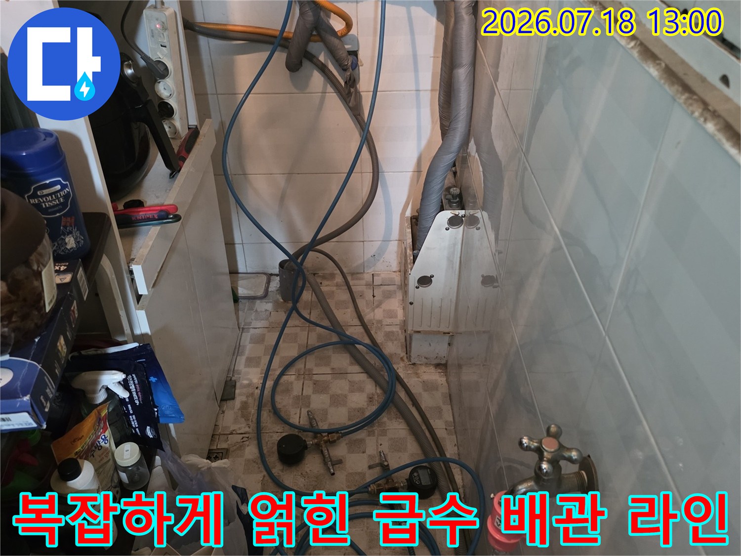 싱크대 하단 벽면에 고정된 수도 밸브와 늘어진 파란색 플라스틱 호스들