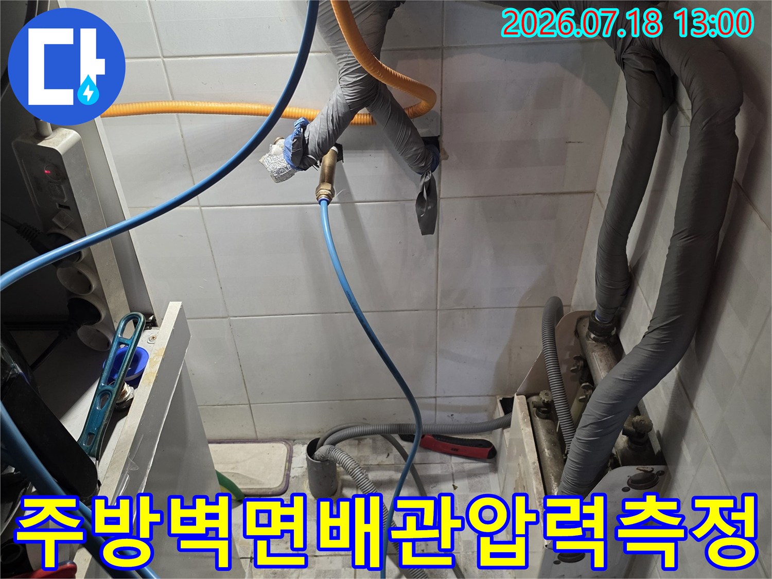 회색 보온재가 씌워진 벽면 배관에 파란색과 노란색 호스가 연결되어 있는 사진
