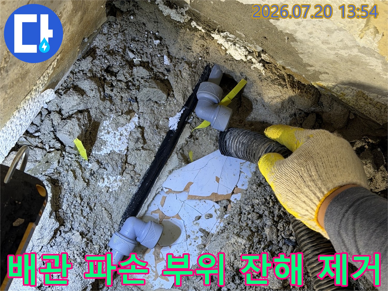 노출된 검은색 수도 배관과 흰색 엘보 연결부-작업자가 흡입 장비로 주변을 청소하는 모습