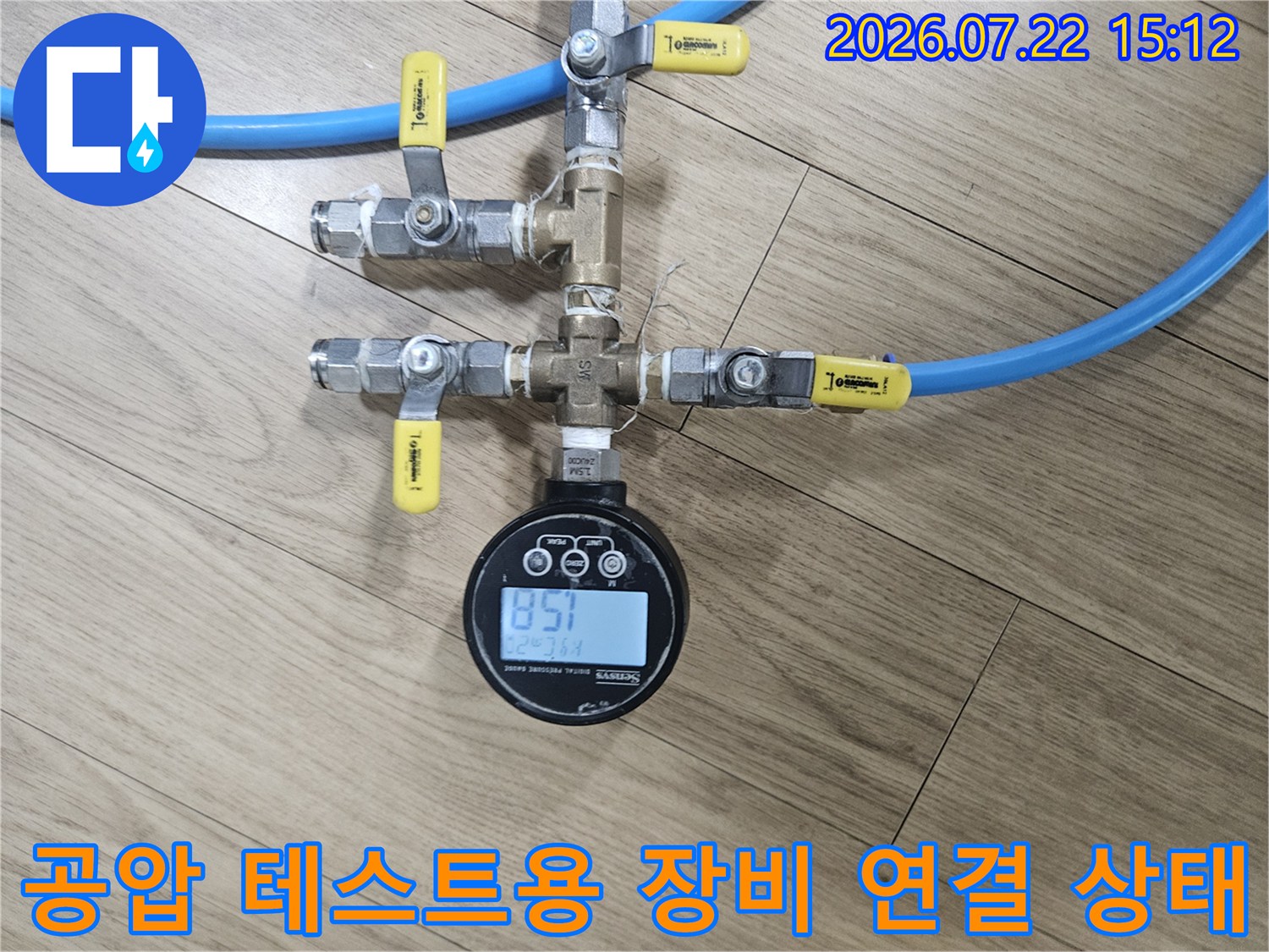 금속 밸브와 파란색 튜브가 연결되어 있고 상단에 수치가 표시된 디지털 게이지가 놓인 사진