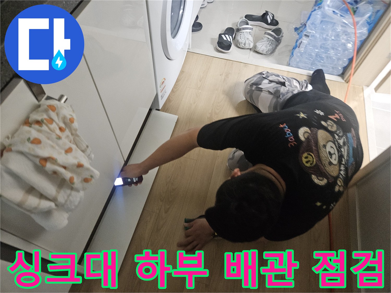 어두운 싱크대 아래쪽 배관 부위를 손전등으로 밝히는 장면