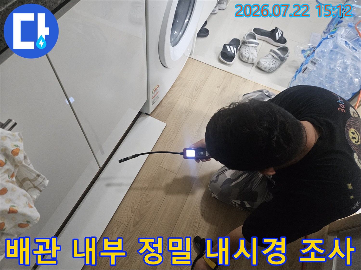 작업자가 무릎을 굽히고 앉아 가구 밑 배관 속으로 내시경 탐지기를 밀어 넣는 장면