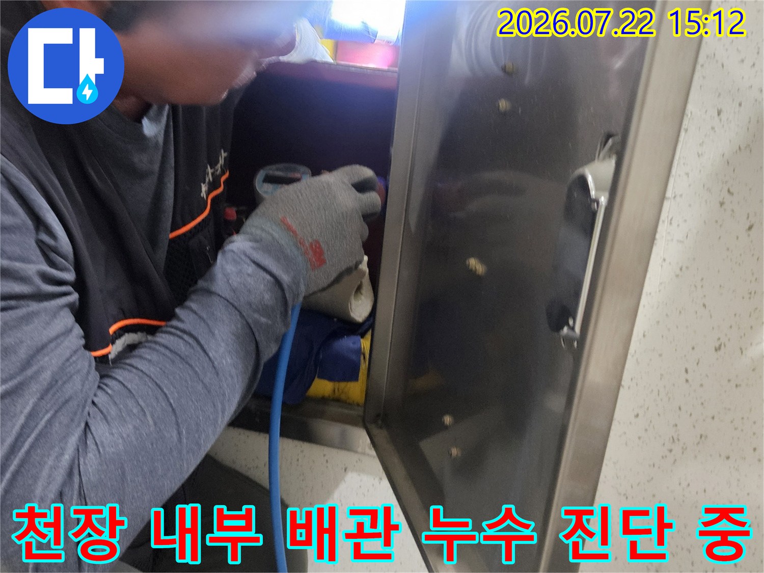 작업자가 천장 마감재 너머의 배관 부위를 가스 탐지 장비로 정밀하게 측정하는 사진