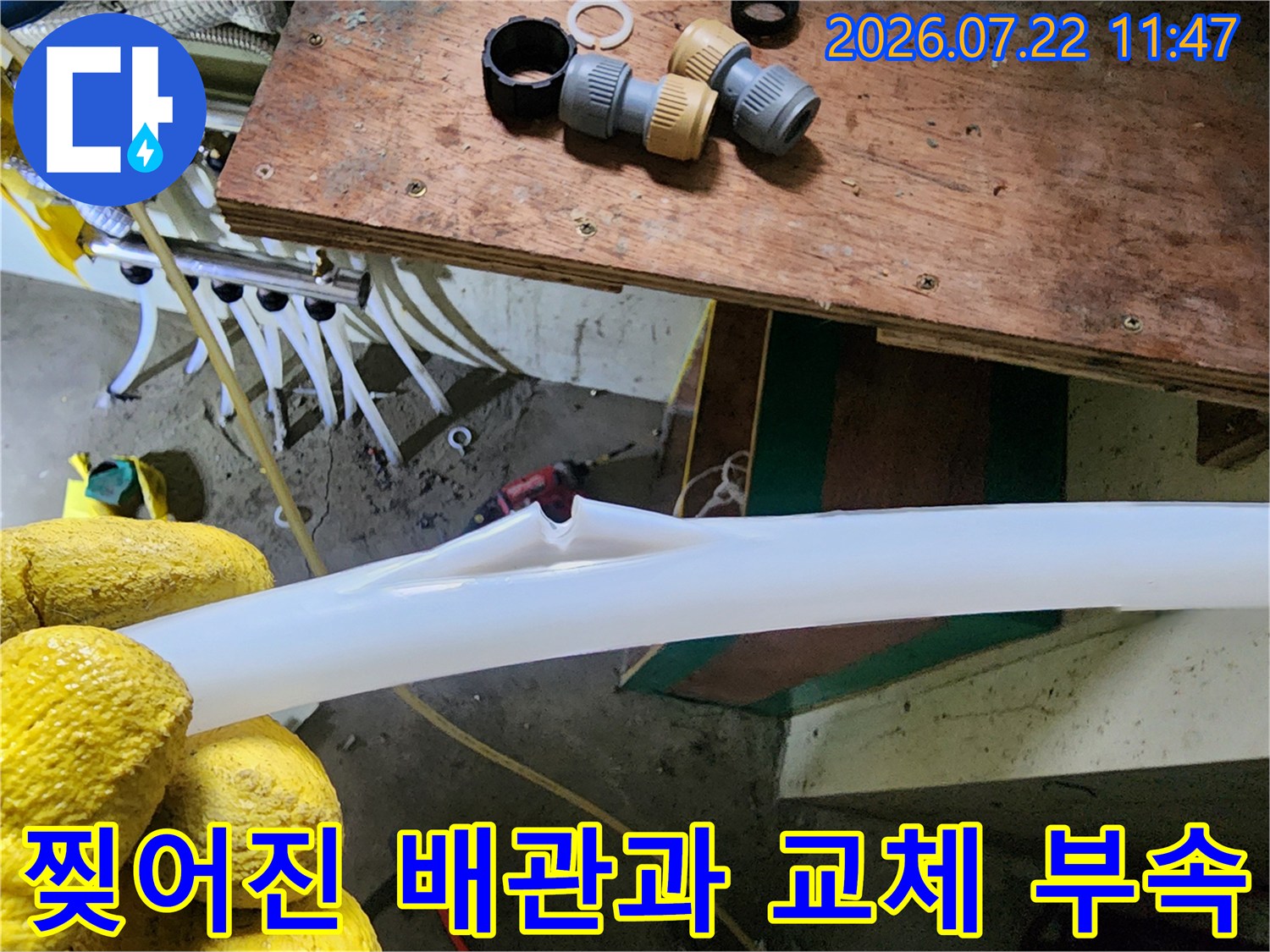 배경에 연결 부속들이 놓여 있고 앞쪽에는 파손되어 갈라진 흰색 배관이 놓인 모습