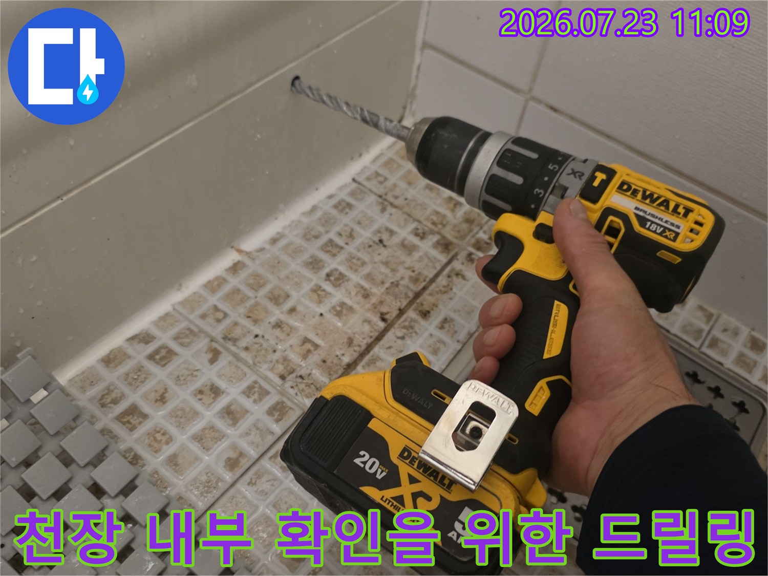 화장실 타일 천장 부근에 전동 공구를 사용하여 구멍을 뚫고 있는 현장 사진