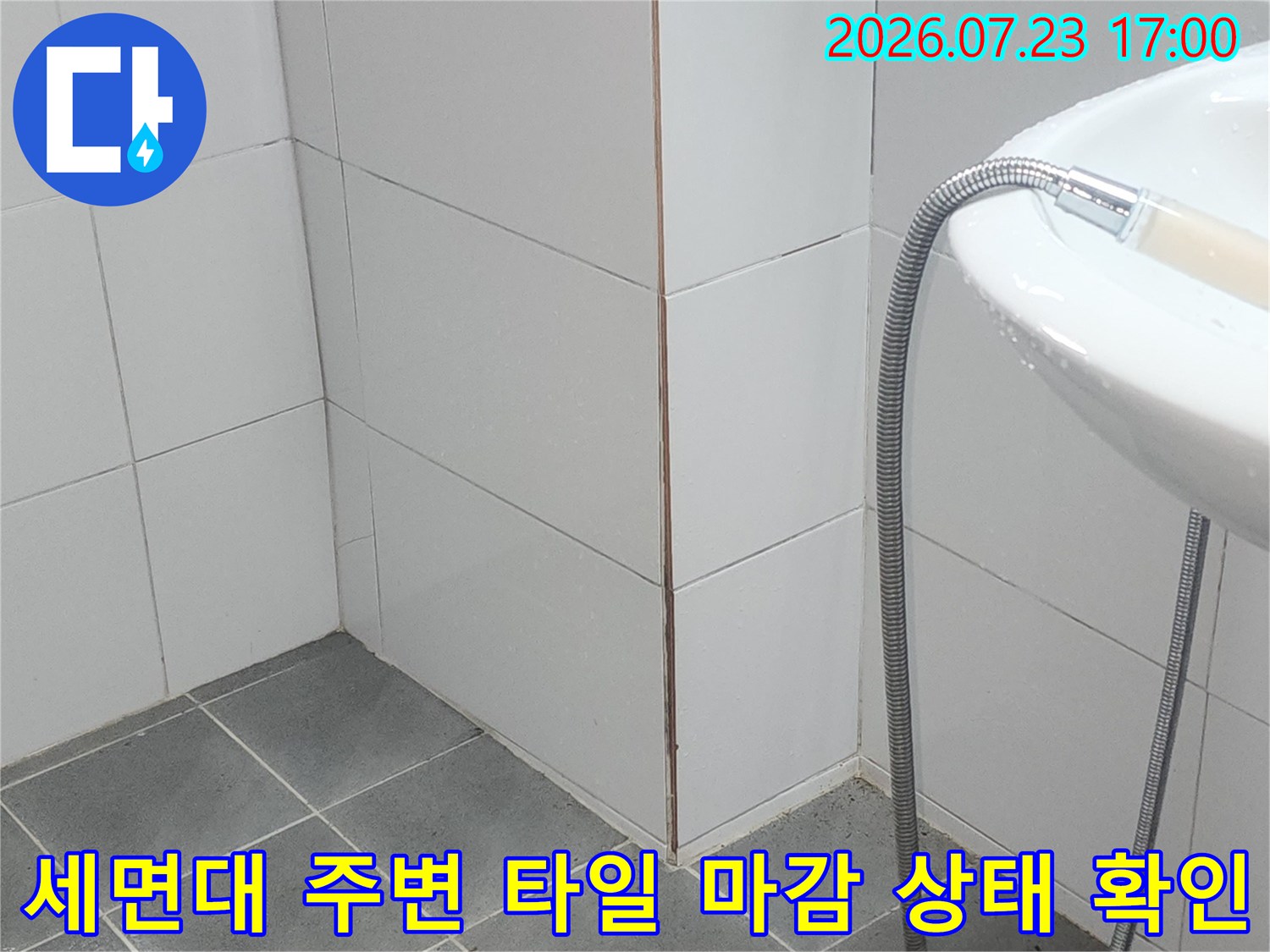 흰색 욕실 타일 벽과 바닥이 만나는 지점에 세면대가 설치되어 있고 샤워기가 연결된 모습