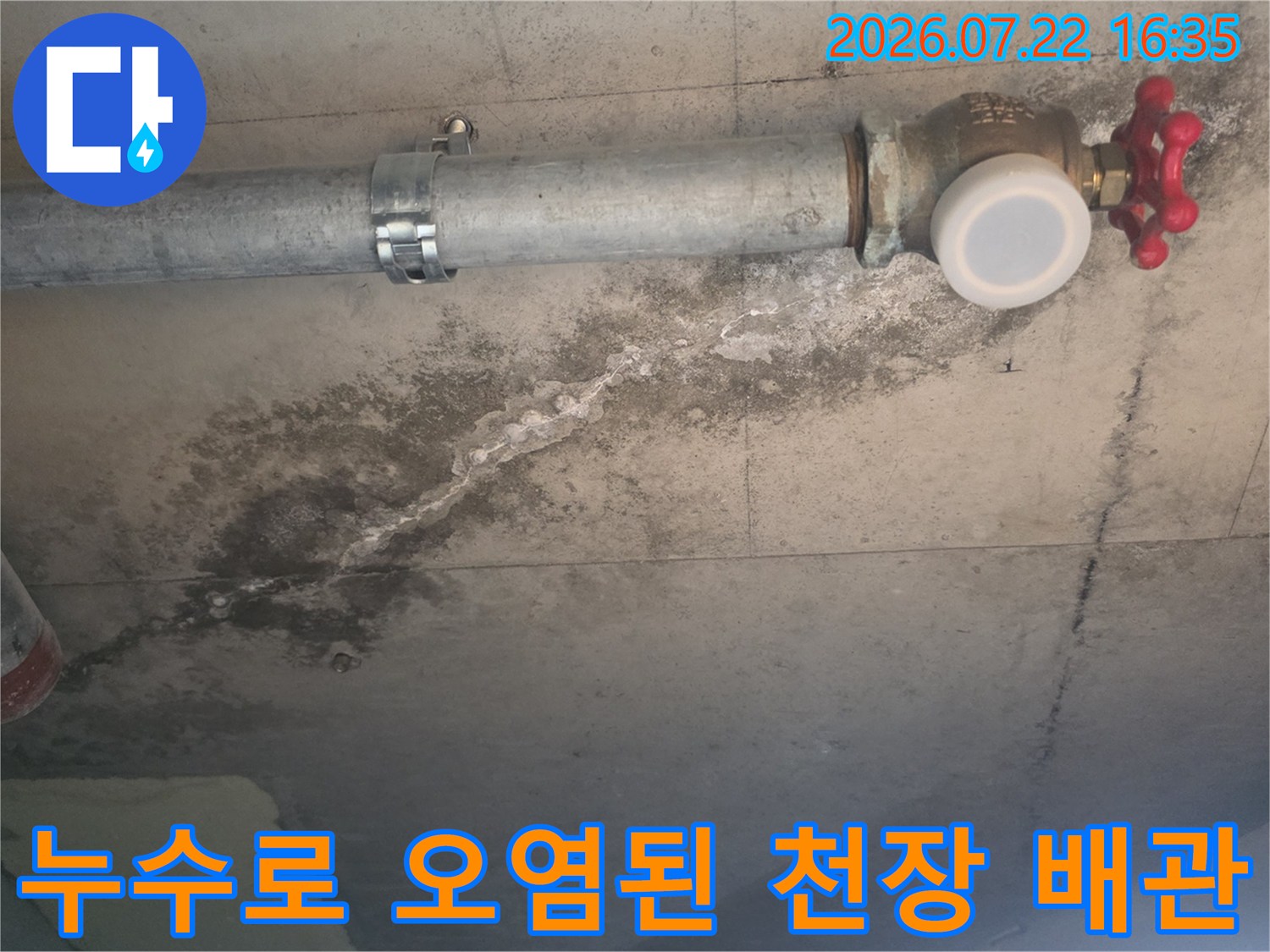 빨간색 밸브가 달린 수도 배관 아래로 누수 피해가 발생하여 거뭇하게 변한 천장 표면