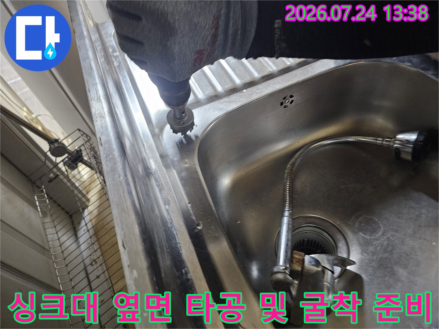 스테인리스 싱크대 옆쪽의 바닥 마감재를 전동 드릴로 제거하고 있는 작업 모습