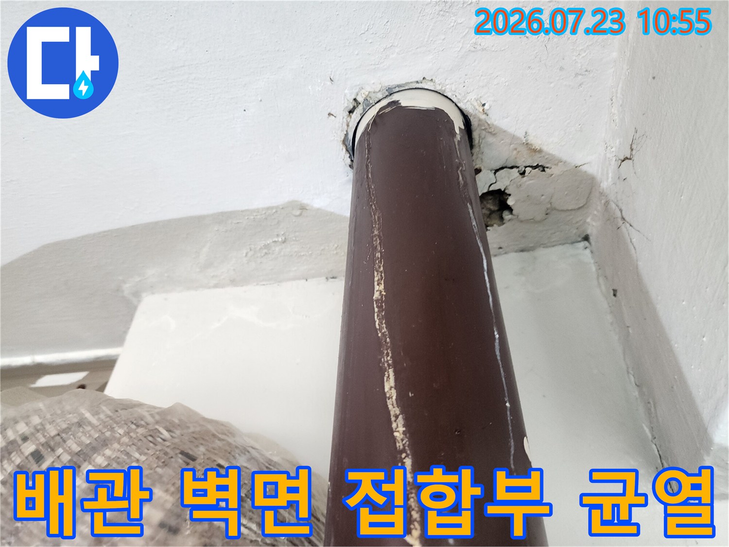 벽을 통과하는 갈색 온수 배관 주위에 발생한 수직 균열과 빈 공간