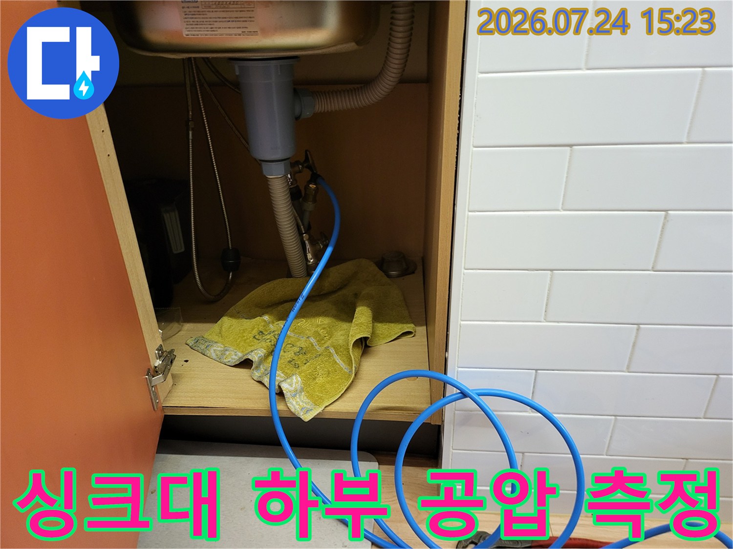 파란색 압력 호스가 싱크대 아래 수도 배관에 연결되어 누수 여부를 판단하는 장면
