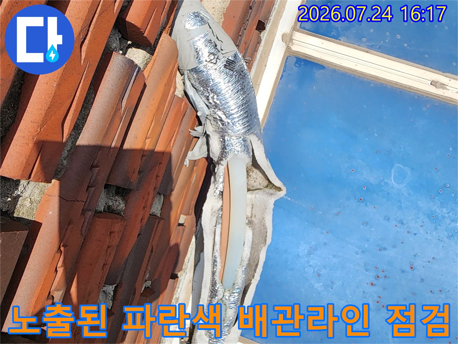 붉은 기와 형태 벽면과 노출된 파란색 보온재로 덮인 긴 수송배관