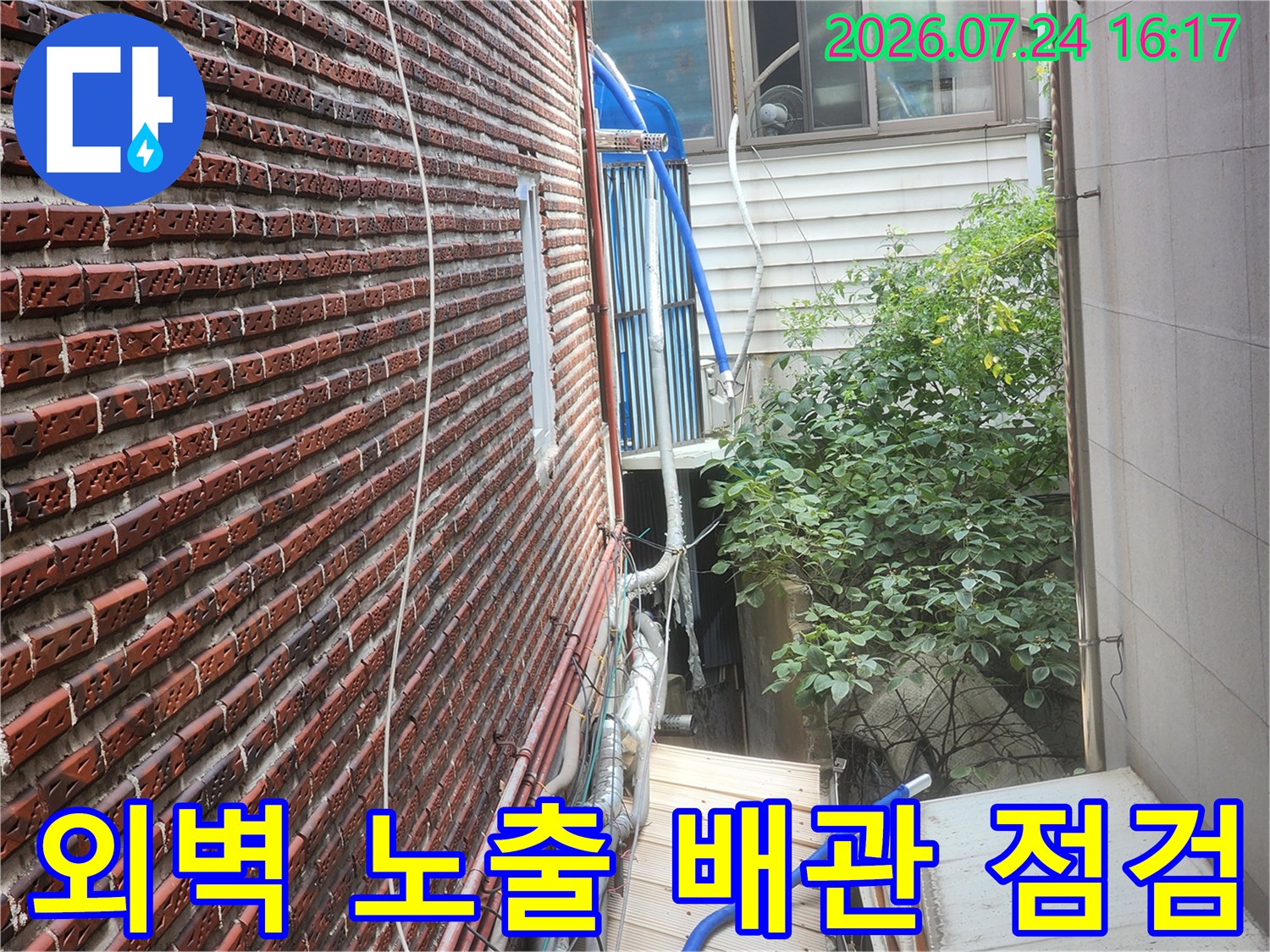 붉은 벽돌 외벽에 설치된 파란색 보온재와 은색 단열재가 덮인 수도 배관 라인