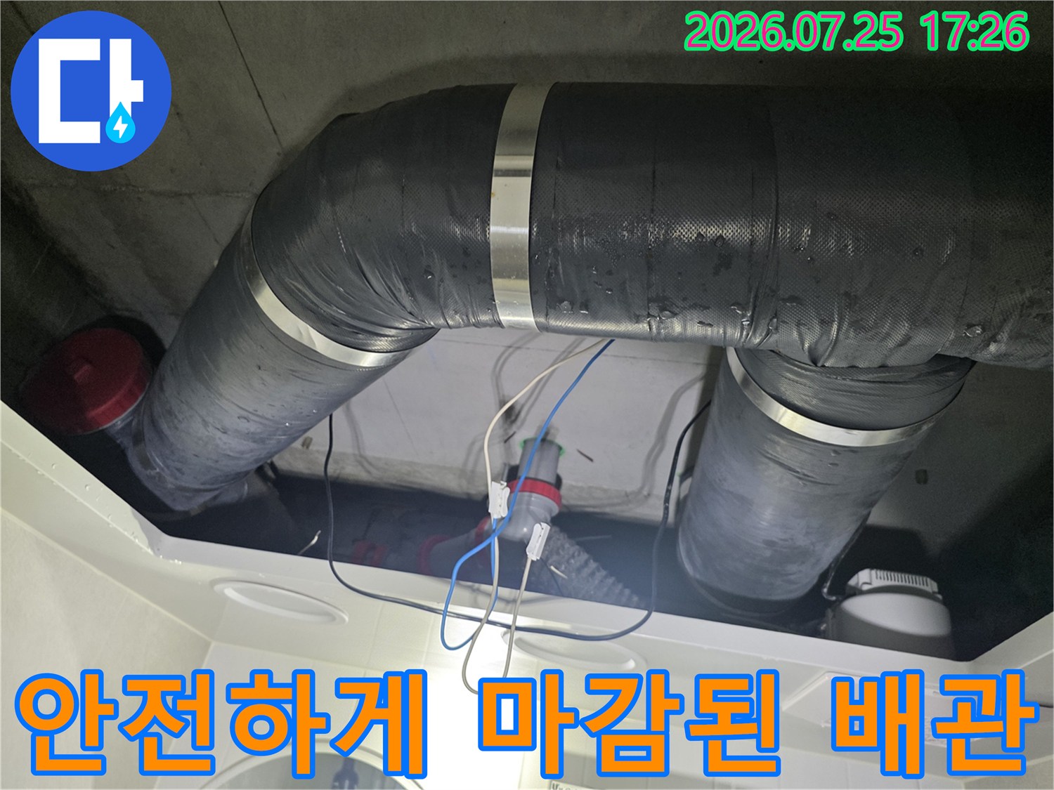 회색 단열 소재로 덮여있고 연결부가 보강된 긴 천장형 배관입니다.