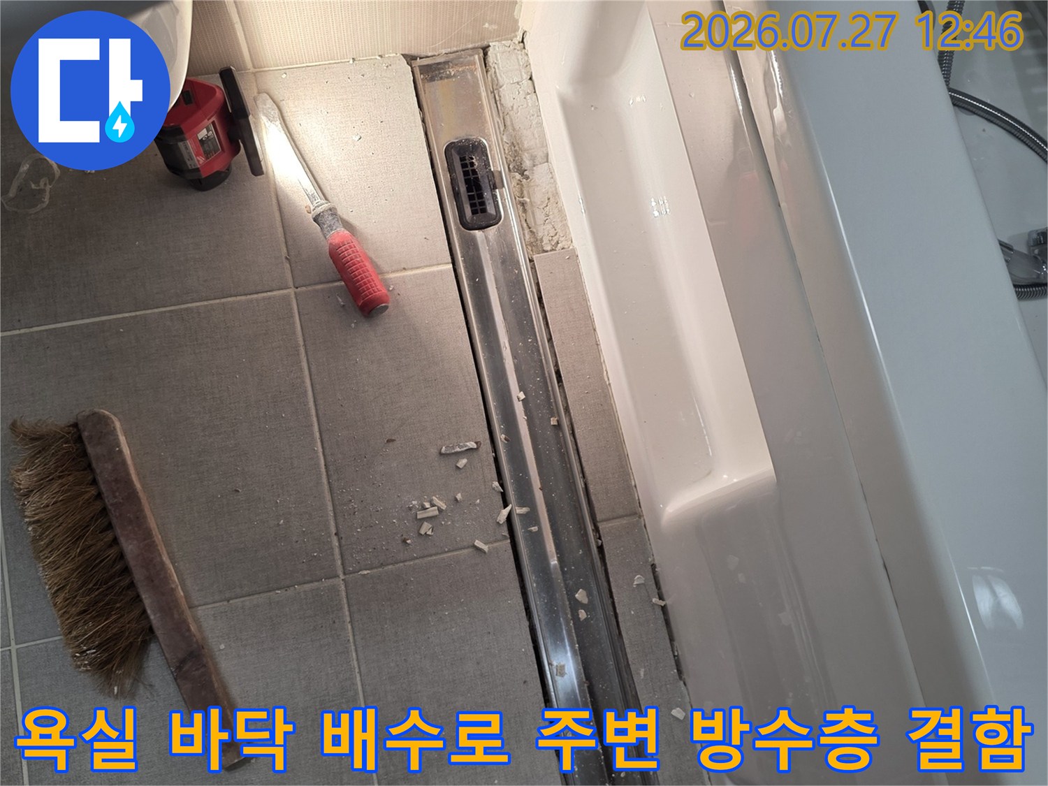길쭉한 형태의 욕실 트랜치 배수구와 그 옆에 놓인 빨간색 손잡이 도구 및 청소용 브러시