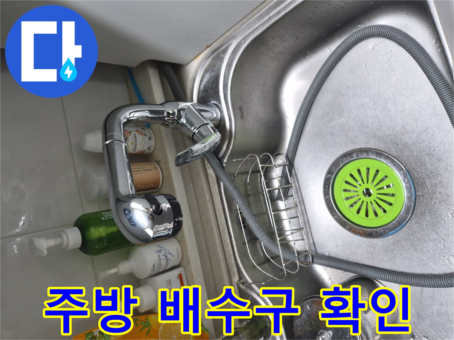 스테인리스 싱크대 볼과 수전 호스가 보이는 하부장 내부 모습입니다.