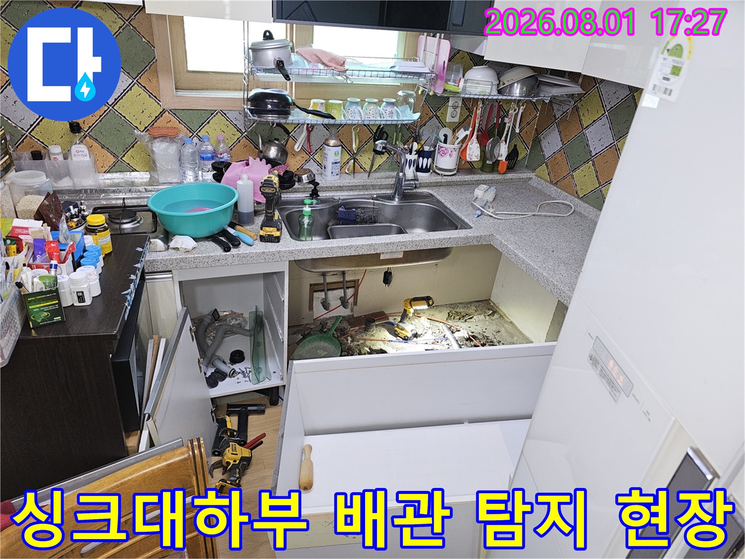 주방 싱크대 하단부로 노출된 수도 배관과 공구들이 배치된 점검 장면
