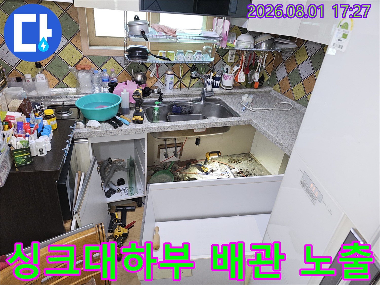 주방 싱크대 하부 공간에서 노출된 배관과 파헤쳐진 바닥 면의 모습