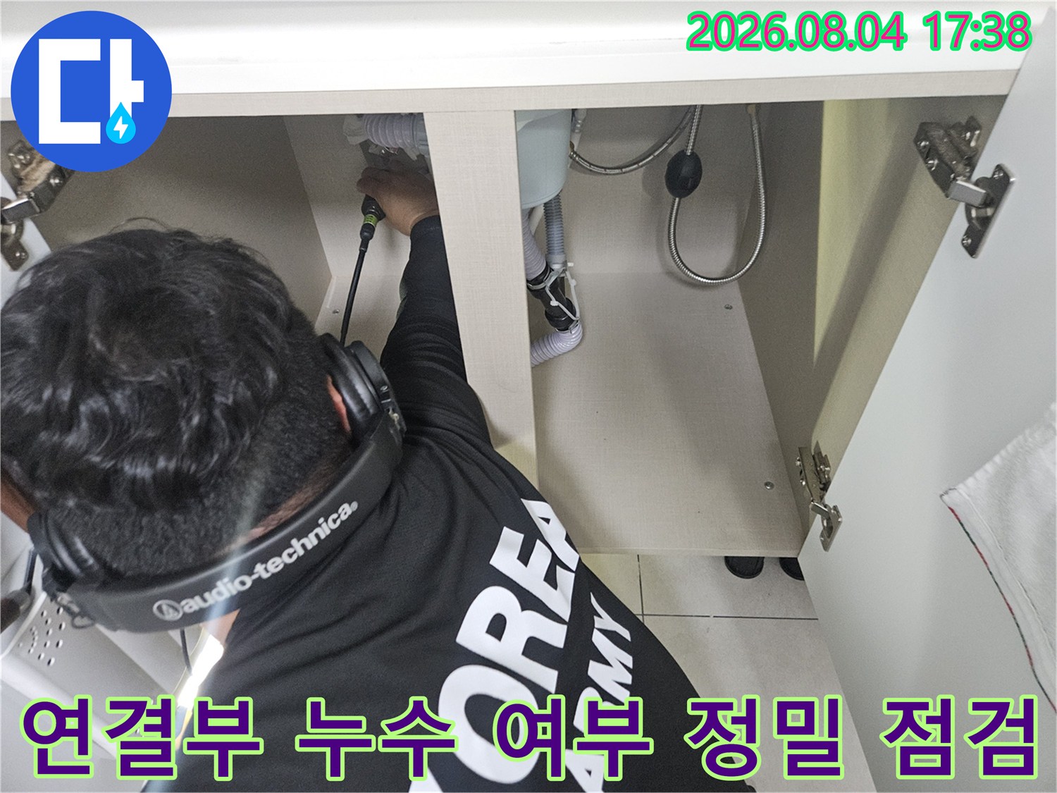 싱크대 하단의 배관 연결 부위와 매립 구간을 고성능 청음 장비로 세밀하게 조사하는 장면입니다.