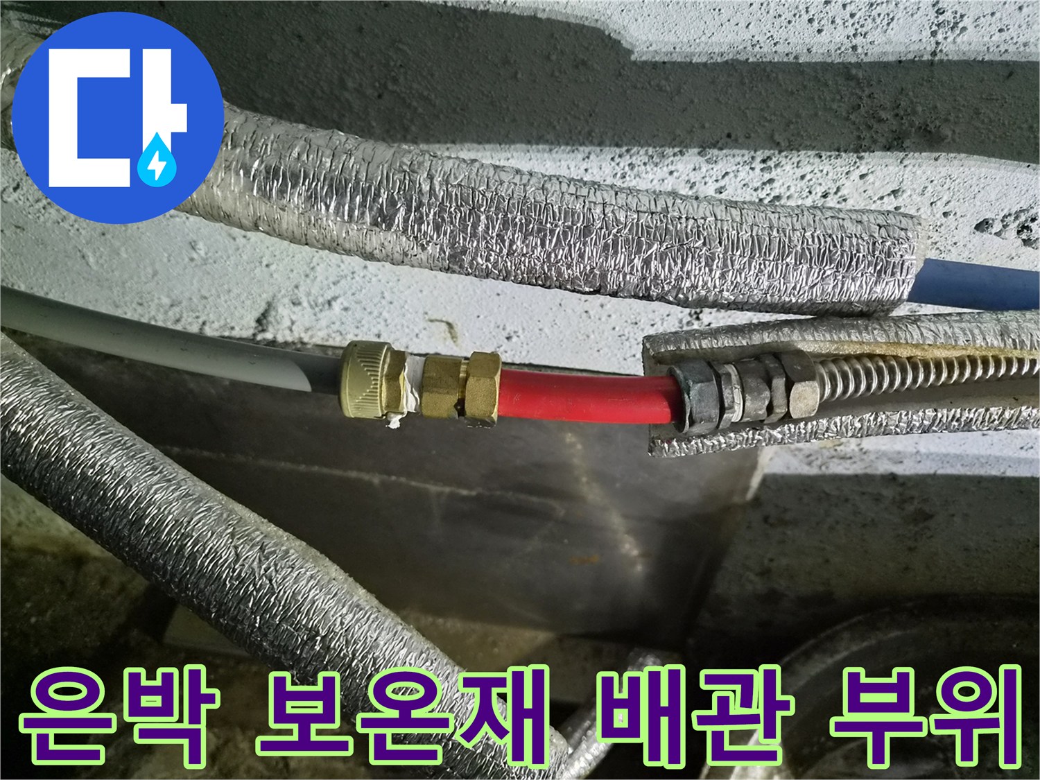 보온재로 덮인 배관의 금속 연결부와 붉은색 호스 근접 촬영