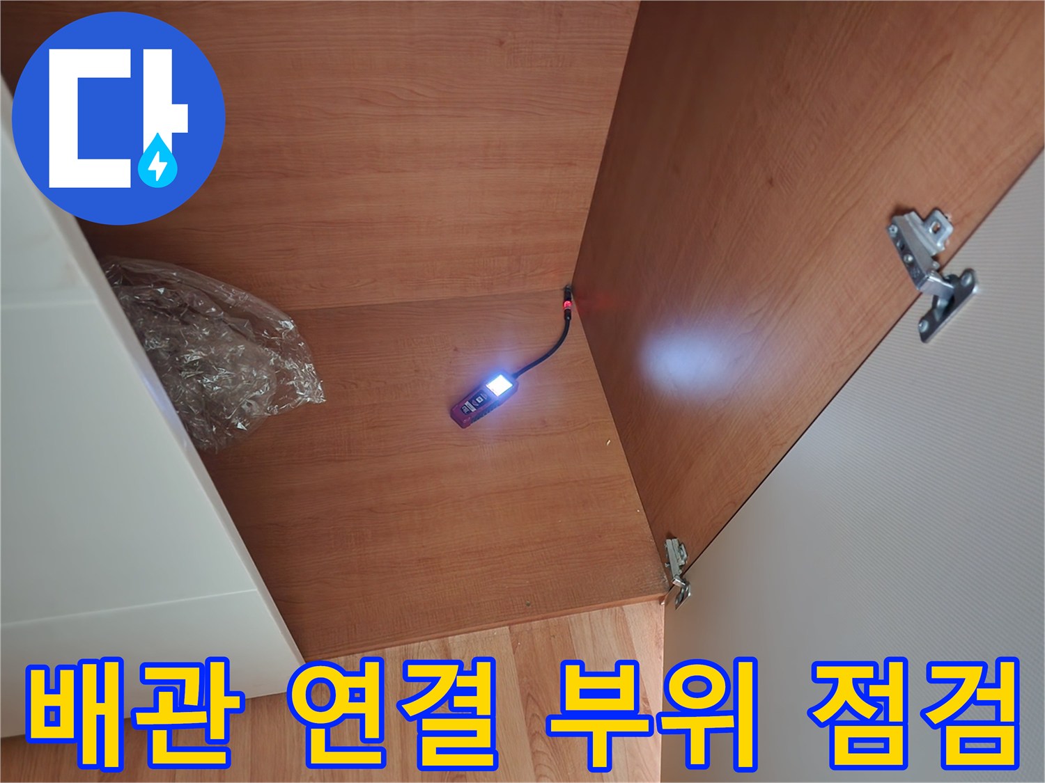 어두운 싱크대 하단 내부를 조명으로 비춰 확인하는 작업 장면